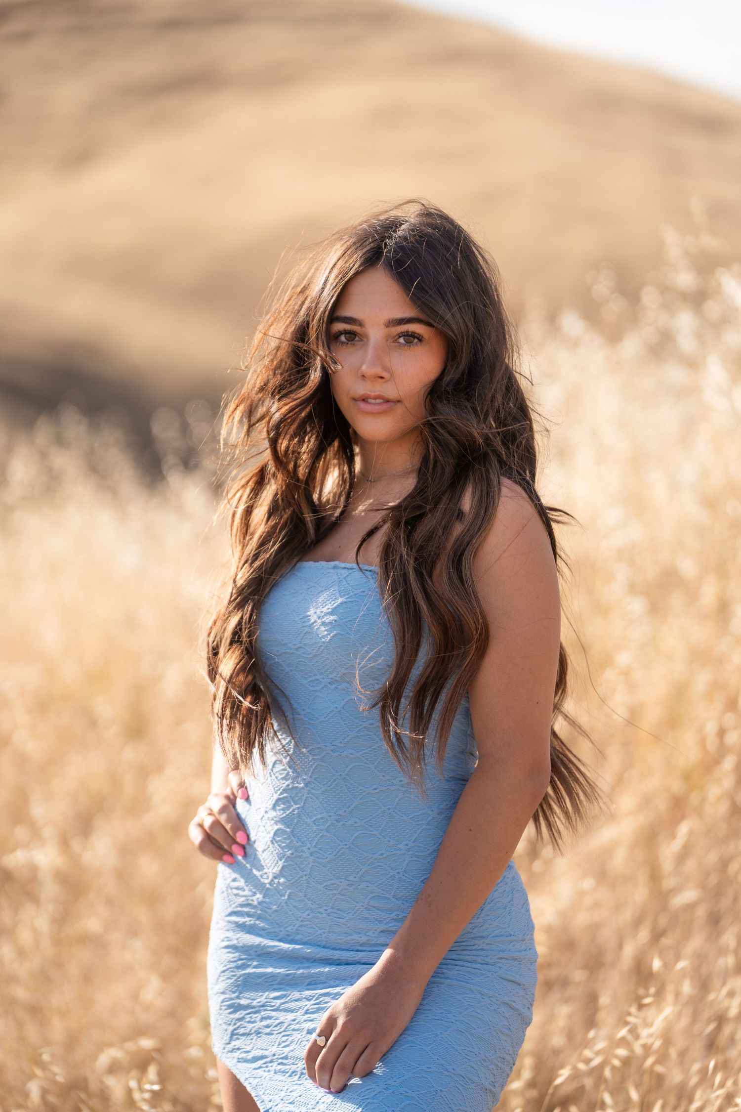 Portrait in light blue dress among sun-lit wheat field during golden hour.