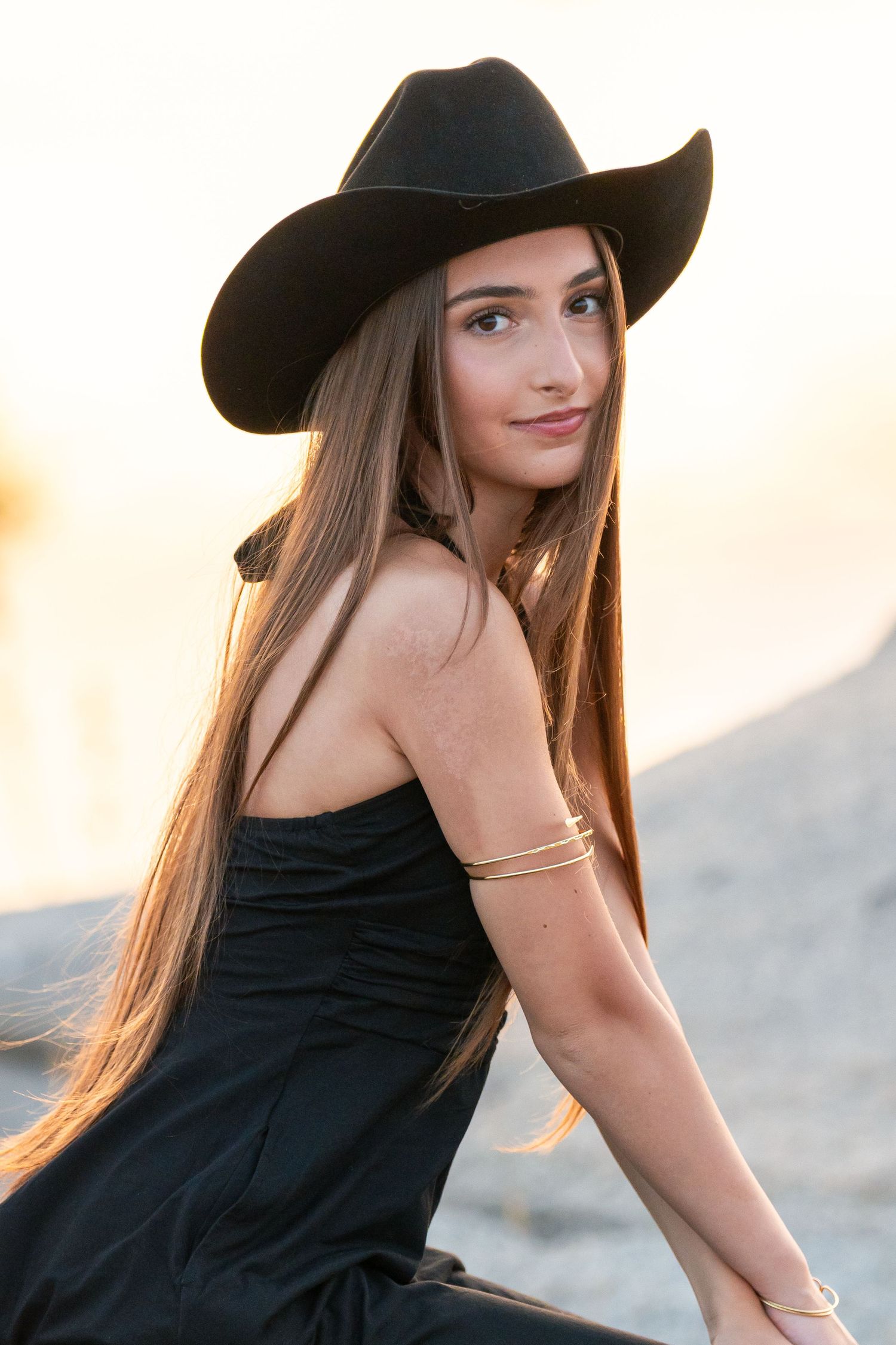 Stylish portraits with black cowboy hat against sunset backdrop.