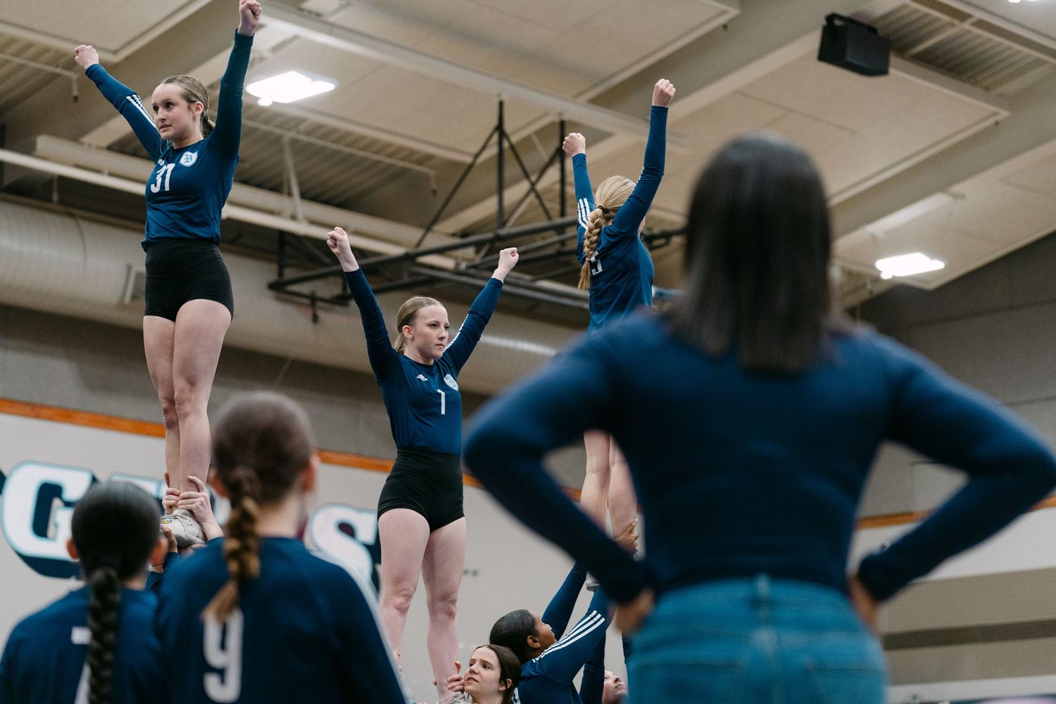 Cheerleaders practicing synchronized jumps and formations in a gymnasium during a training session.