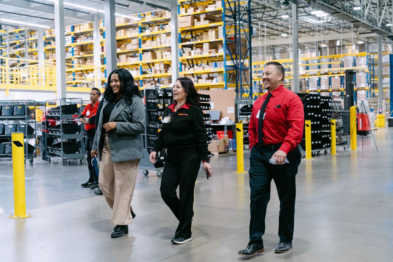 Large warehouse interior with rows of shelves and people walking through a wide aisle in a retail distribution center.