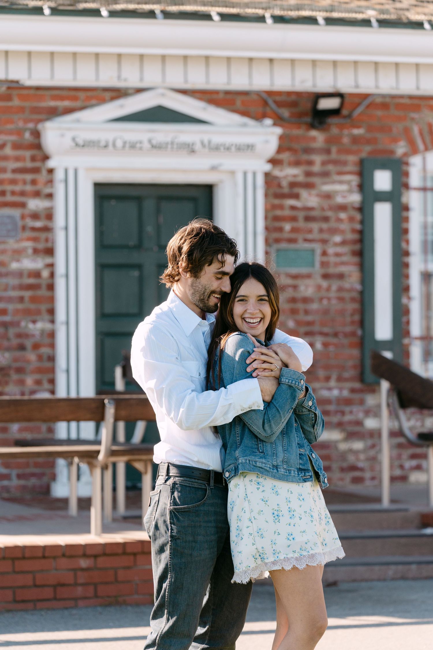 A couple shares tender moments outside a brick building with white trim and green doors.