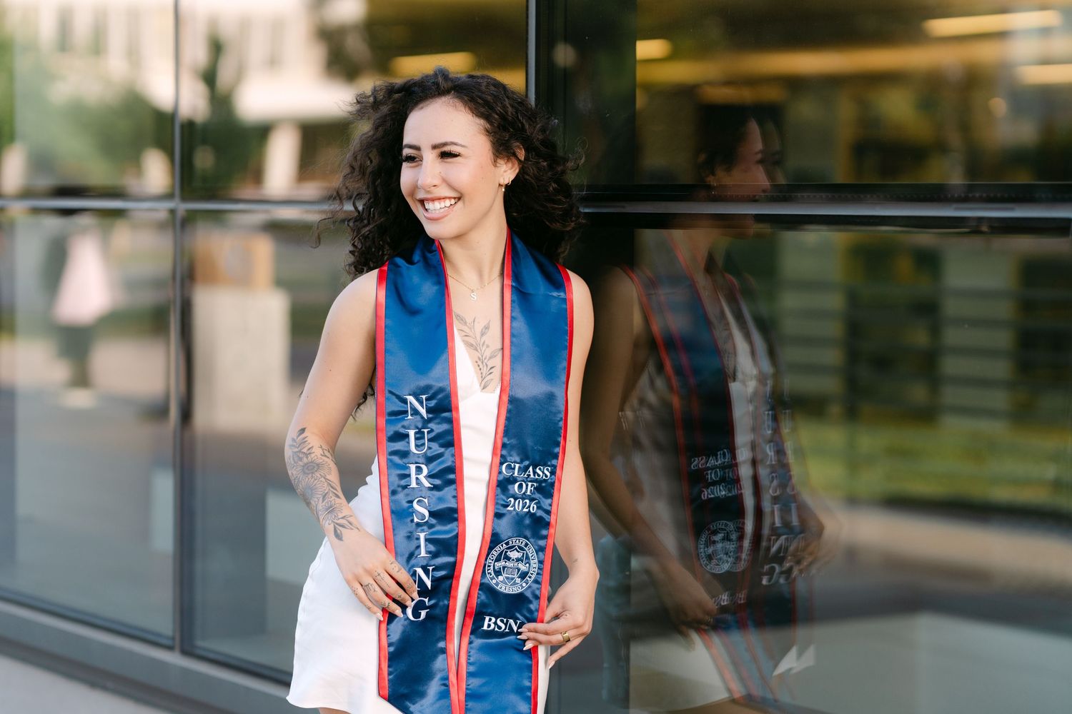 Smiling graduate wearing a blue nursing stole poses outdoors during graduation photo session.