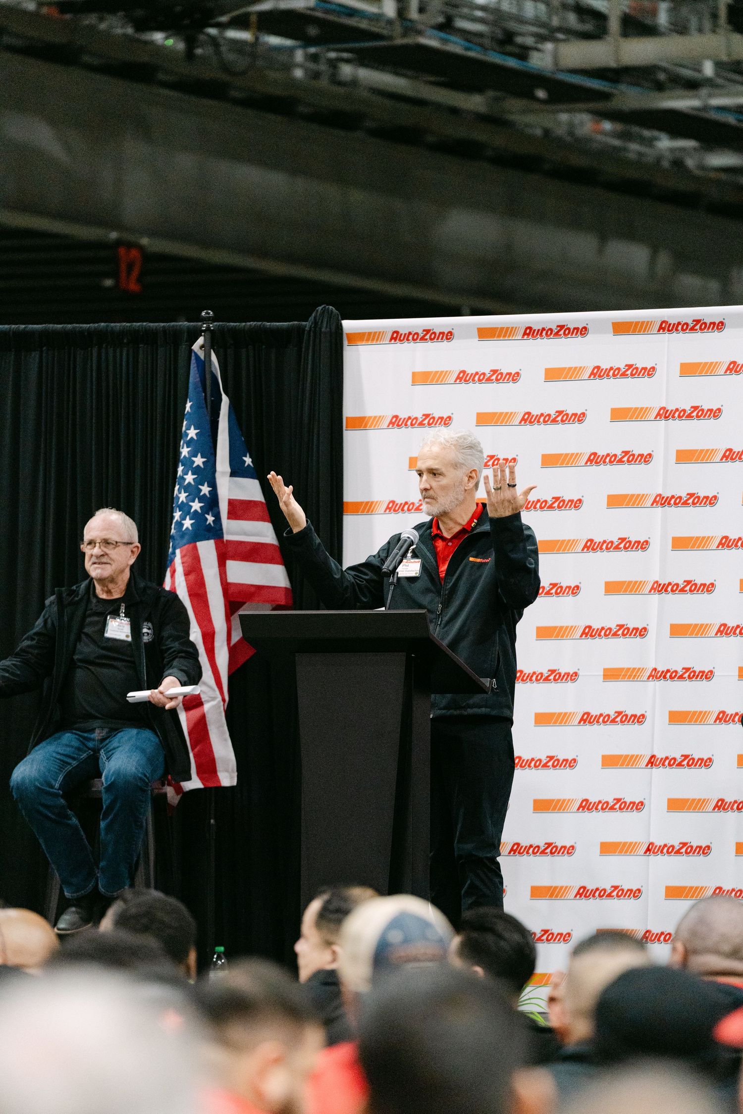 A row of American flags displayed at an event with AutoZone branded backdrop panels.