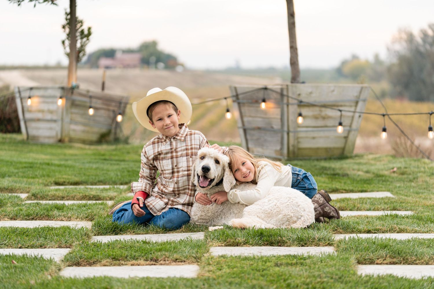 A family relaxes on a blanket in a grassy field with their white dog on a sunny autumn day.