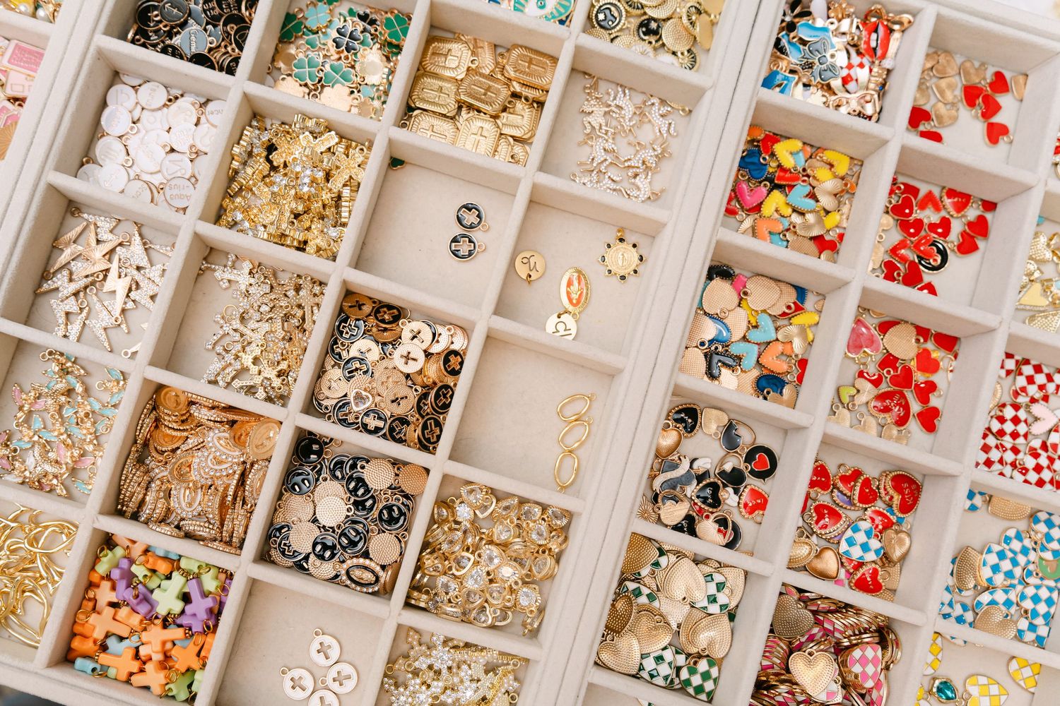 Organized jewelry storage trays filled with colorful beads, charms, and gold earrings sorted in compartments.
