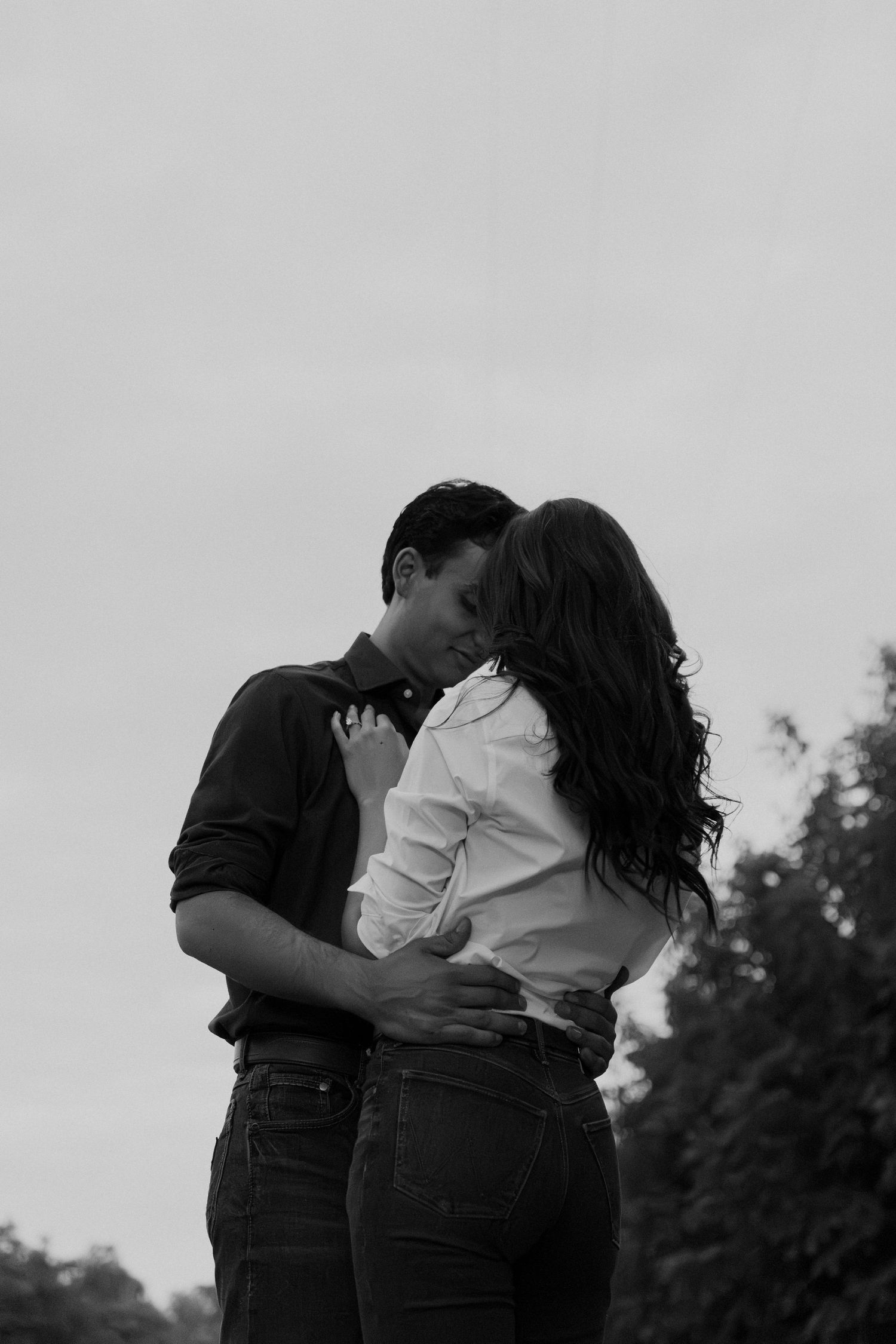 A romantic black and white photo series showing a couple embracing in an outdoor setting with trees in the background.