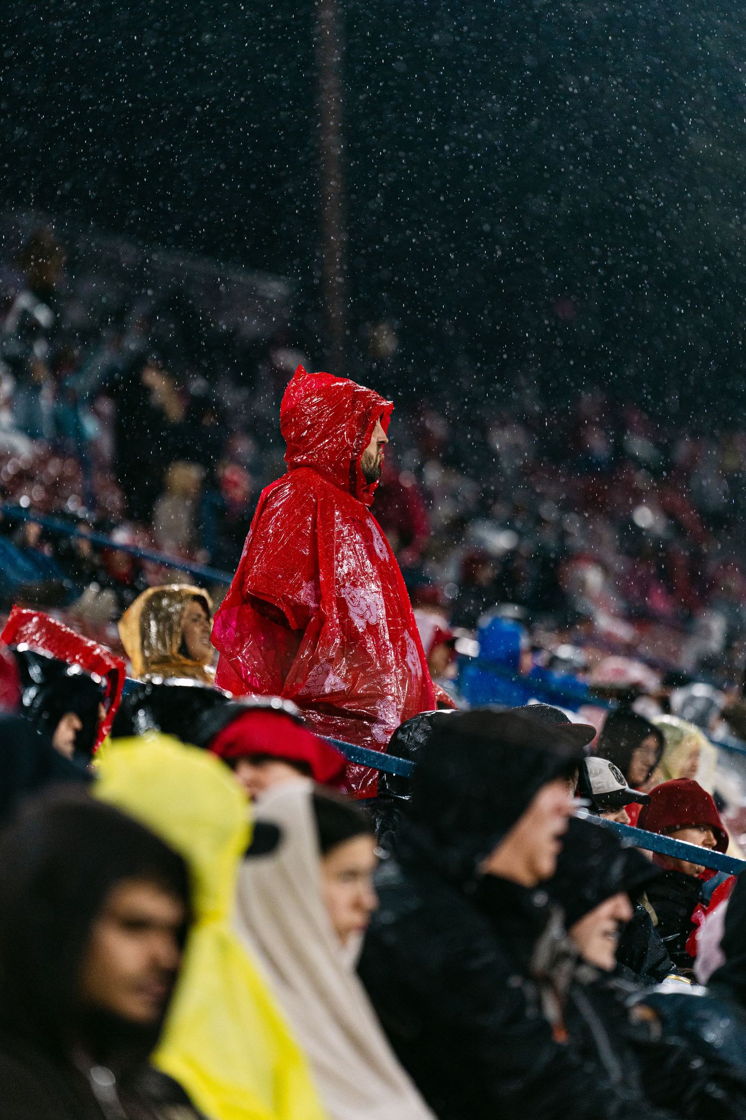 Crowd of spectators wearing rain ponchos in various colors watching an outdoor event in rainy weather.