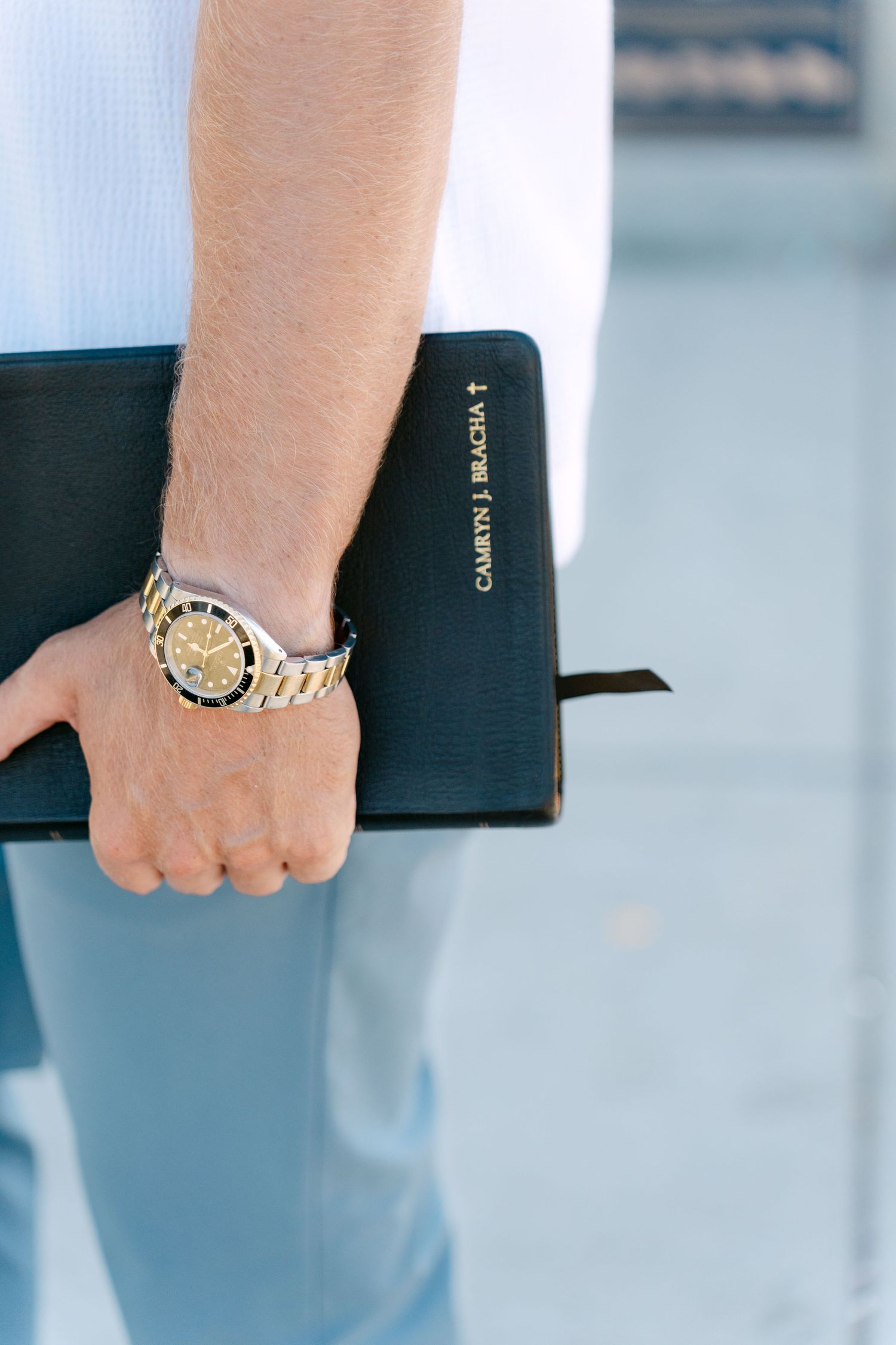Close-up of man holding black leather Bible engraved with name while wearing a gold and silver watch.