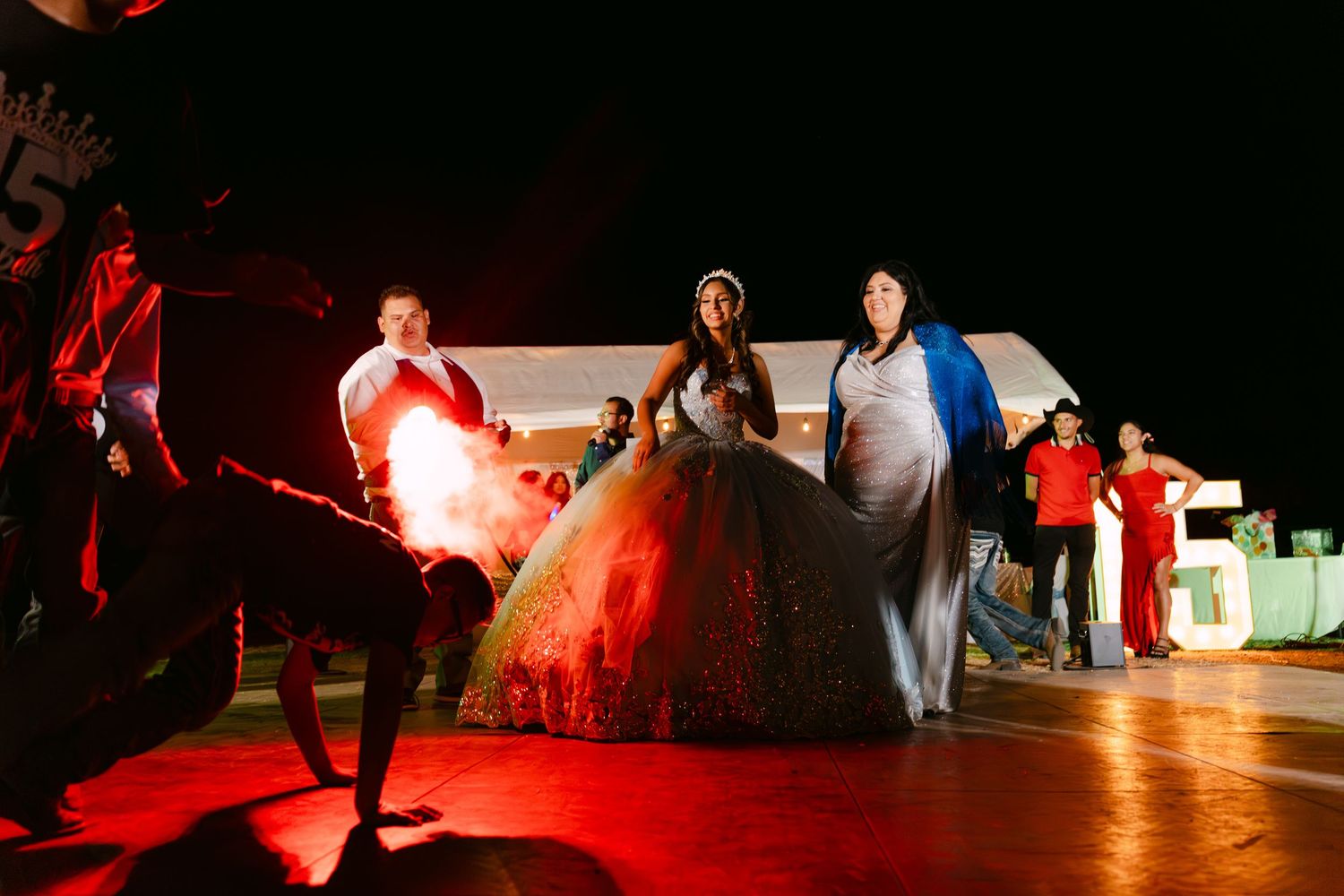 Red-lit dance performance at an outdoor celebration with white tent backdrop.
