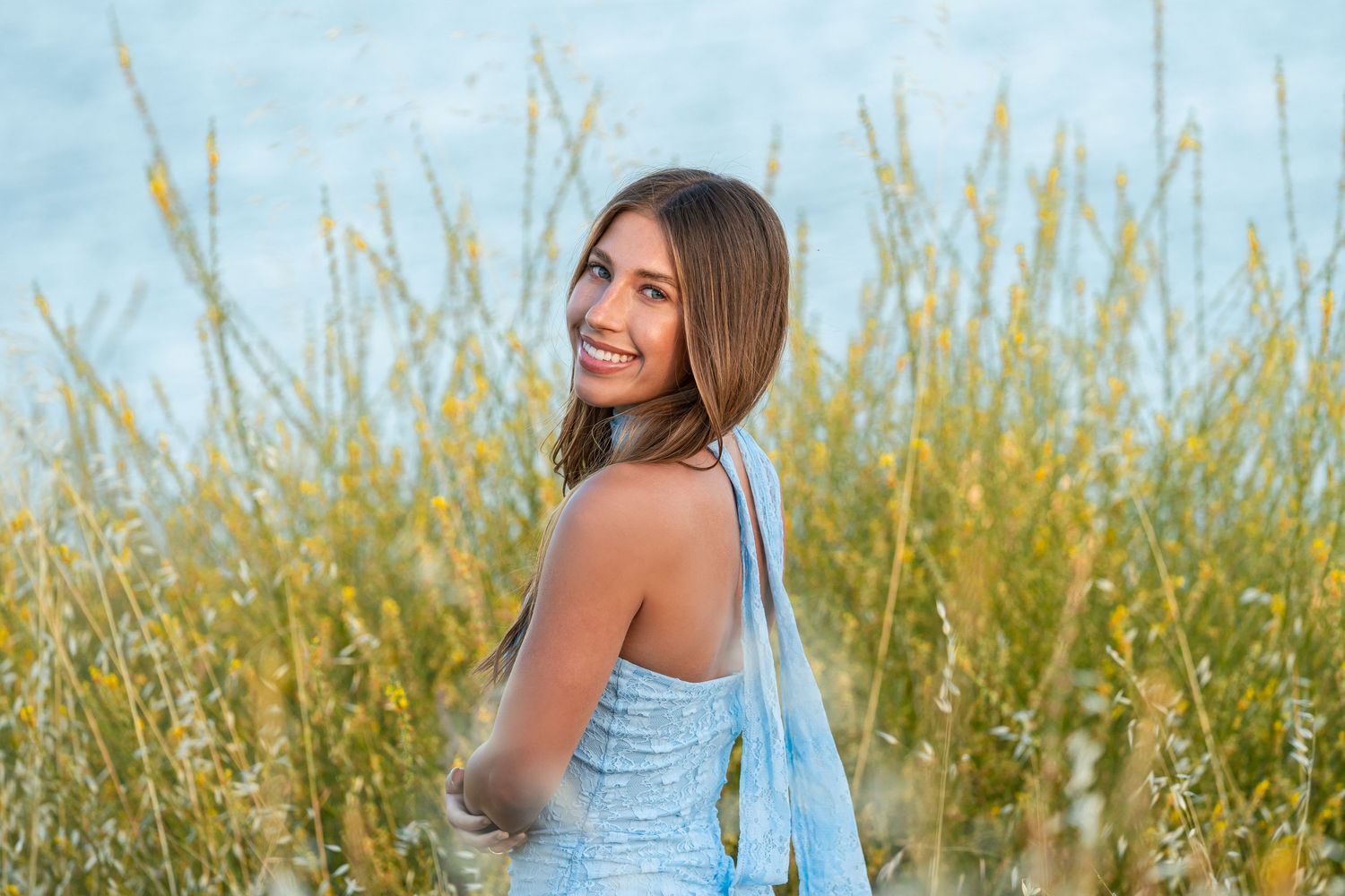 Woman in light blue dress poses in tall grass field during outdoor portrait session.