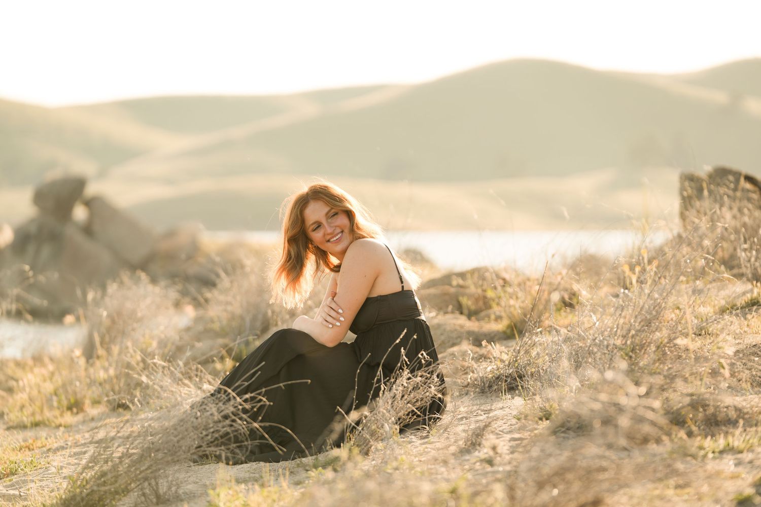 High School Senior in black dress reclining on rocky terrain during sunset.