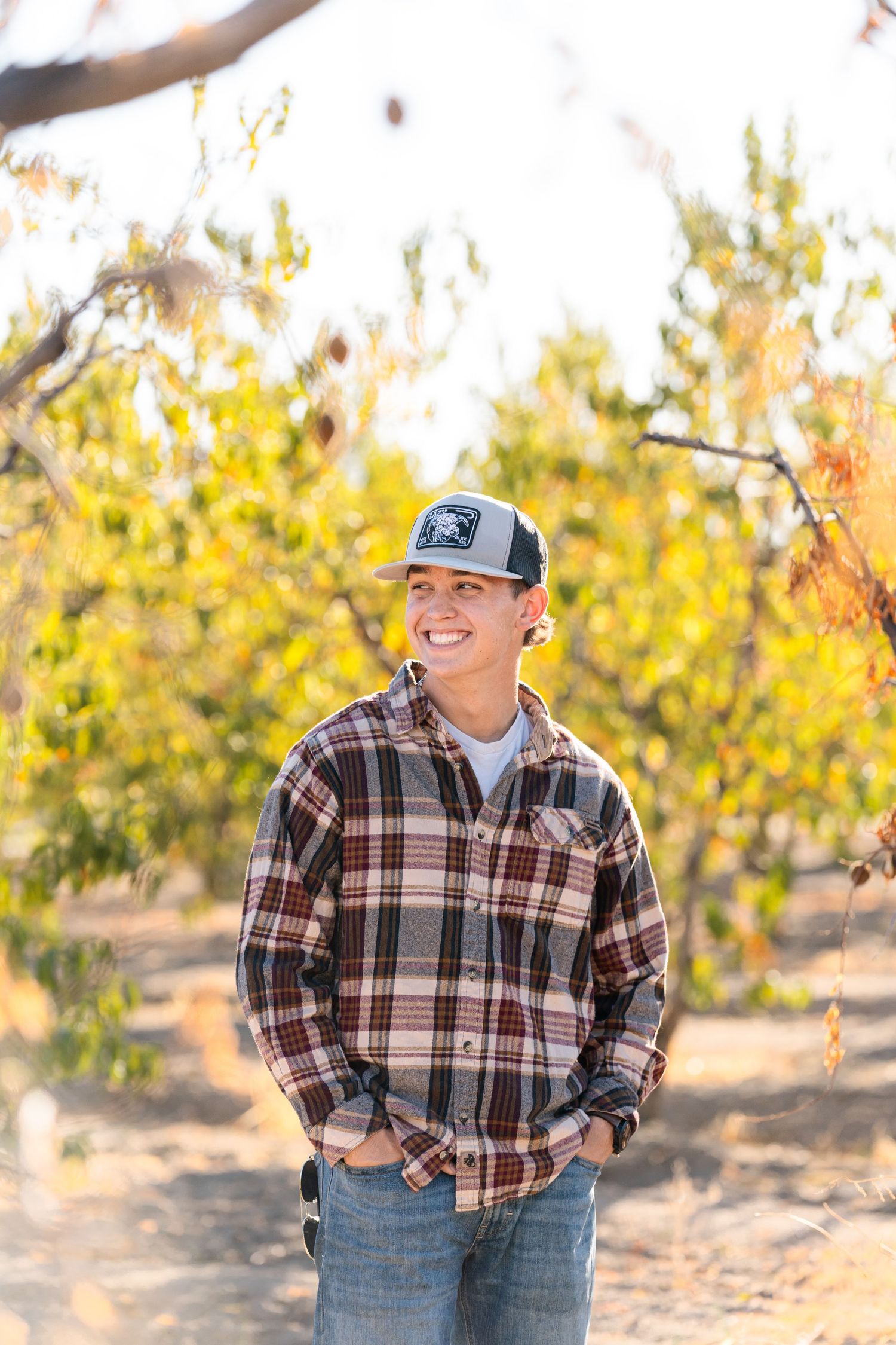Casual outdoor portrait session in a plaid shirt and baseball cap among autumn trees.