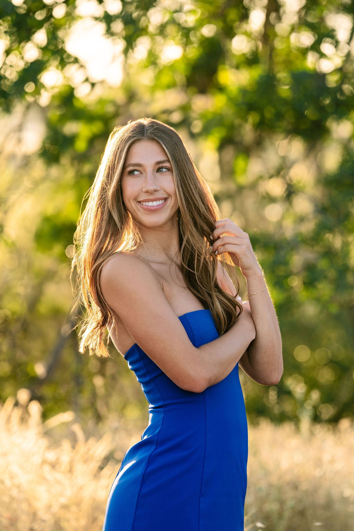 Woman in royal blue dress smiles during sunset photoshoot with bokeh background.