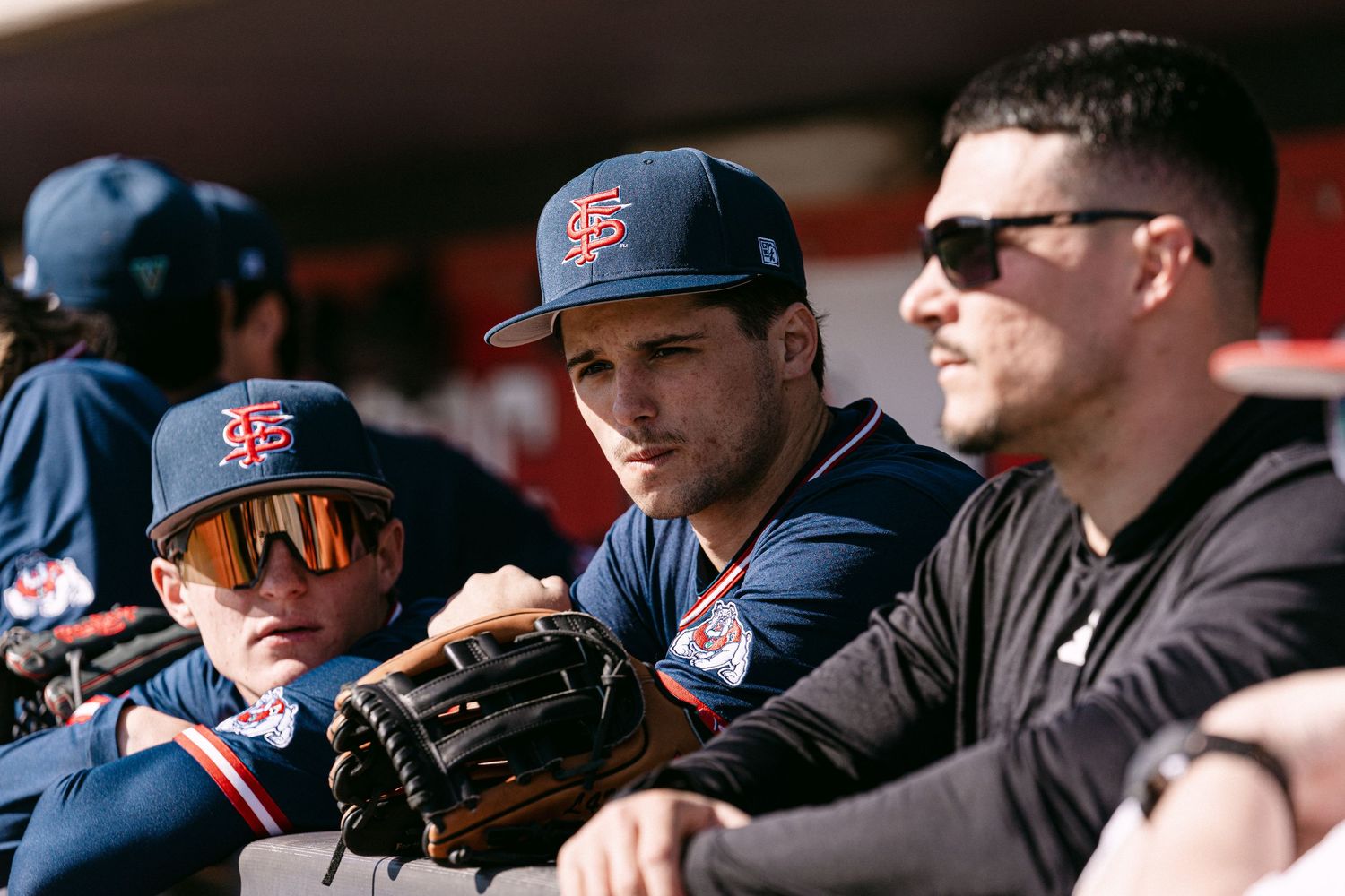 Baseball players and fans in navy blue uniforms and caps watch intently from the dugout during a game.