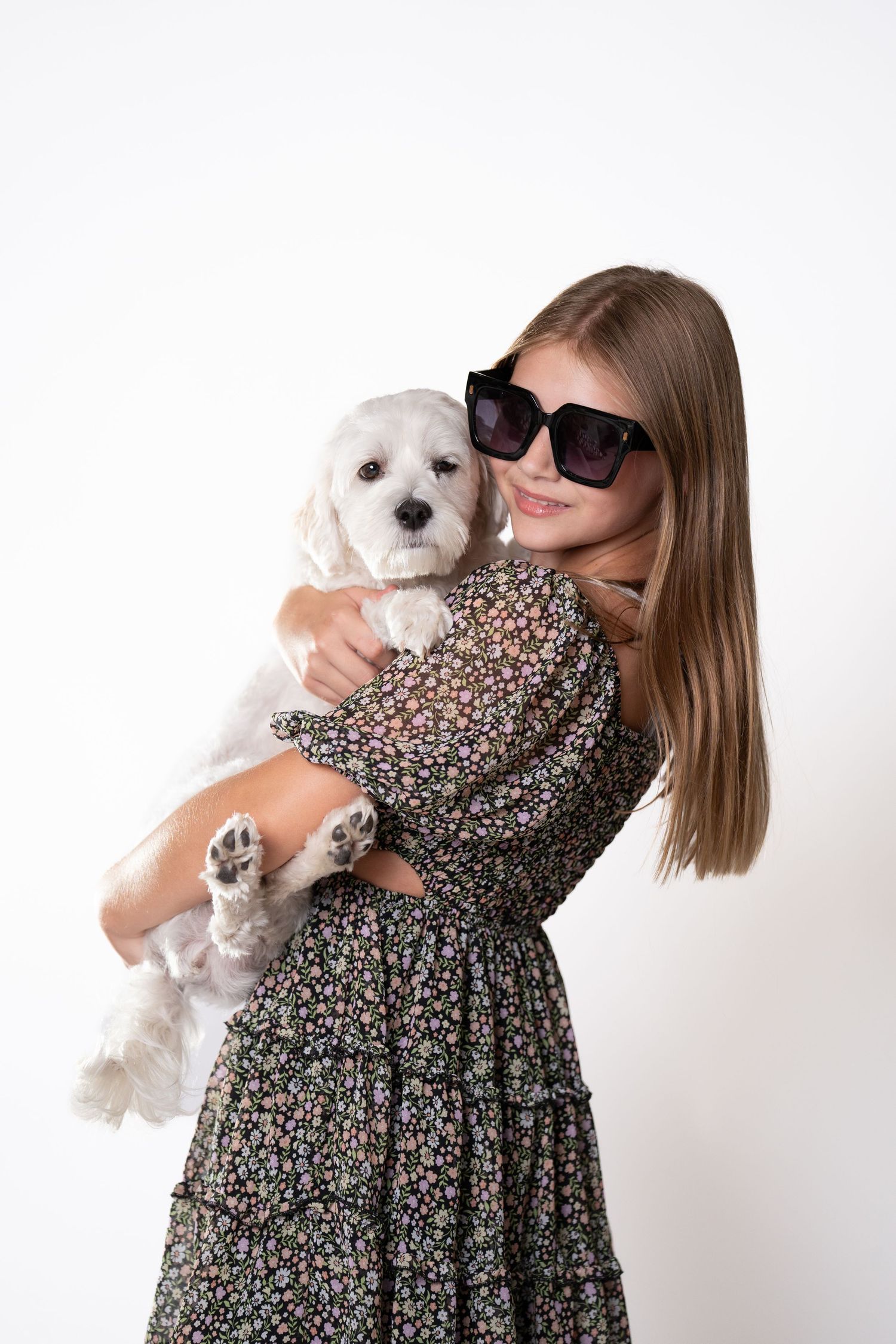 Person in floral dress holding small white puppy against white background.