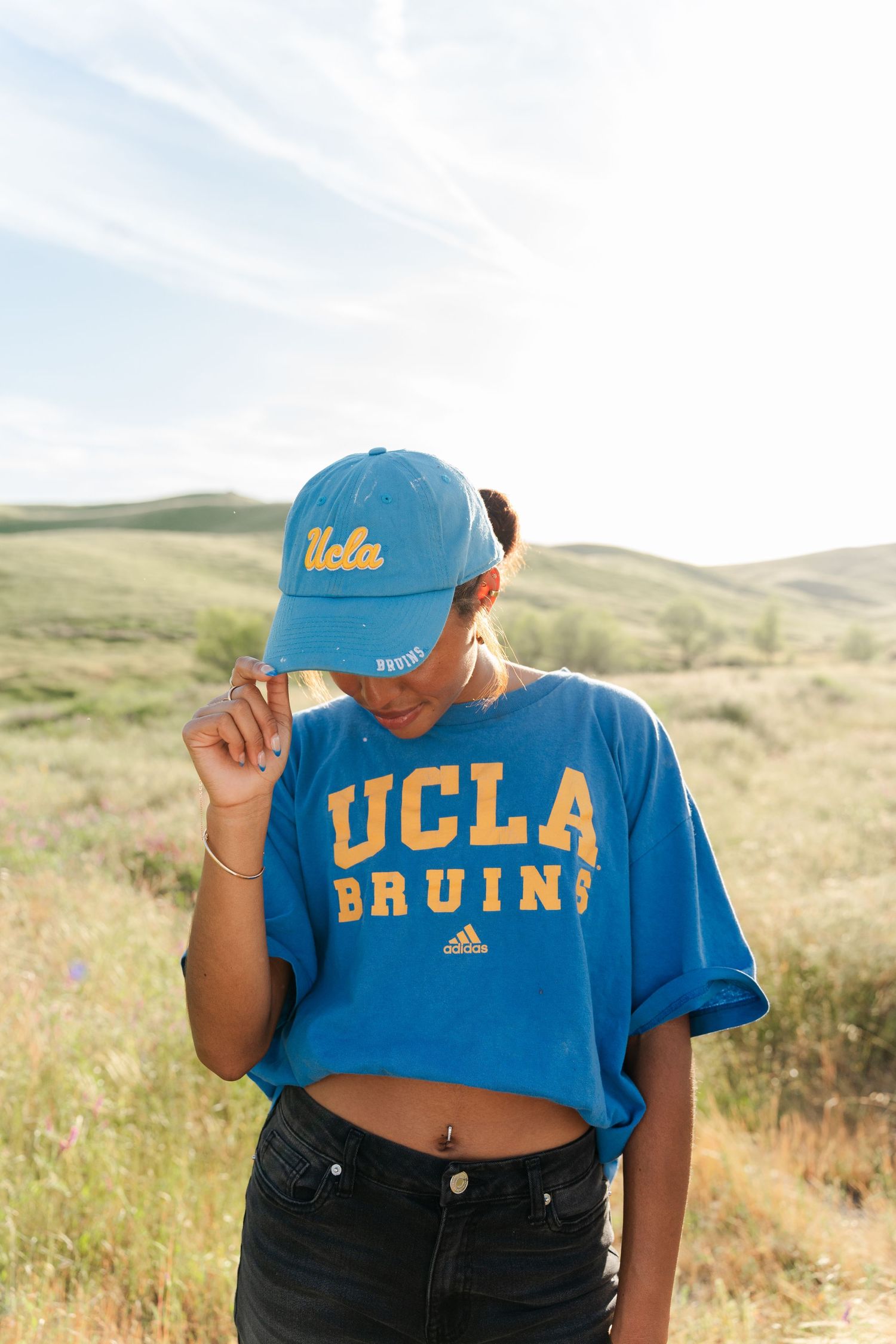 Person wearing UCLA Bruins cropped t-shirt and dark pants poses against rolling hills in outdoor setting.