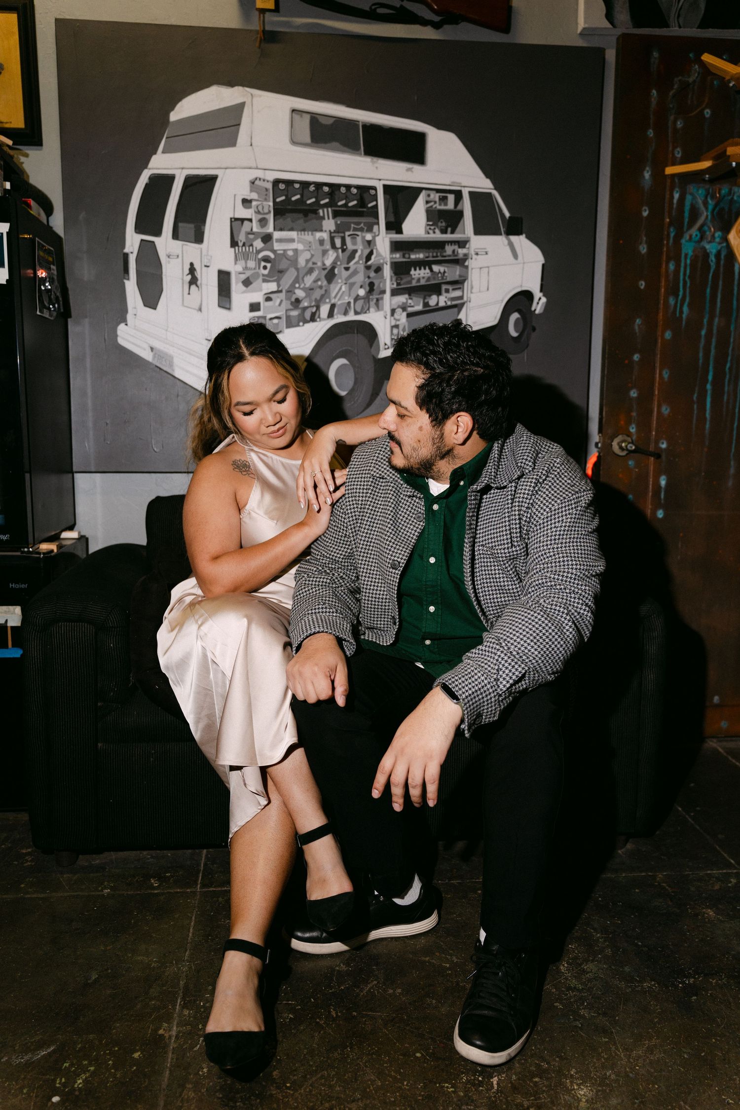 A couple shares an intimate moment on a couch with a vintage van artwork displayed on the wall behind them.
