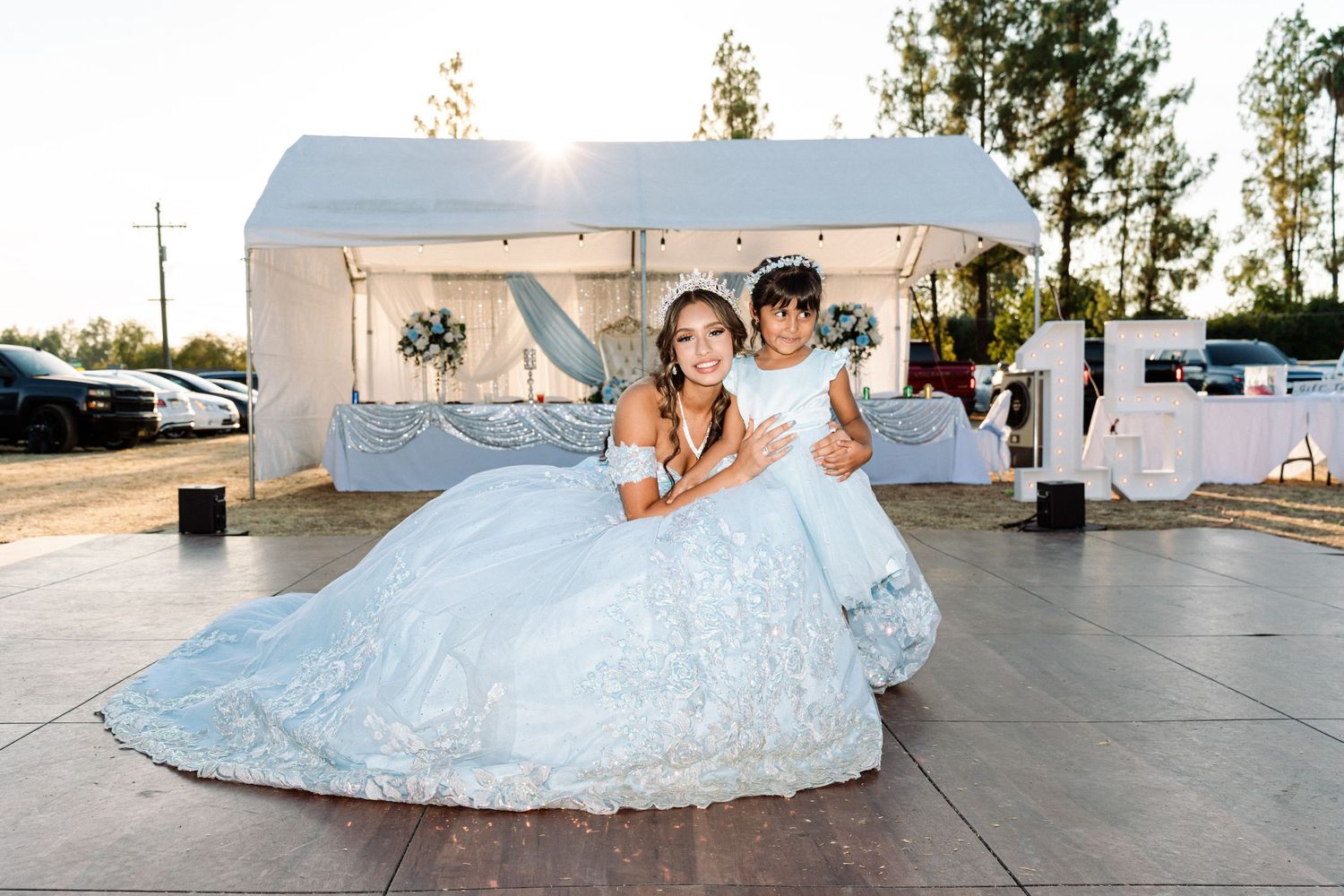 A person in a flowing light blue ballgown poses for photos at an outdoor venue.