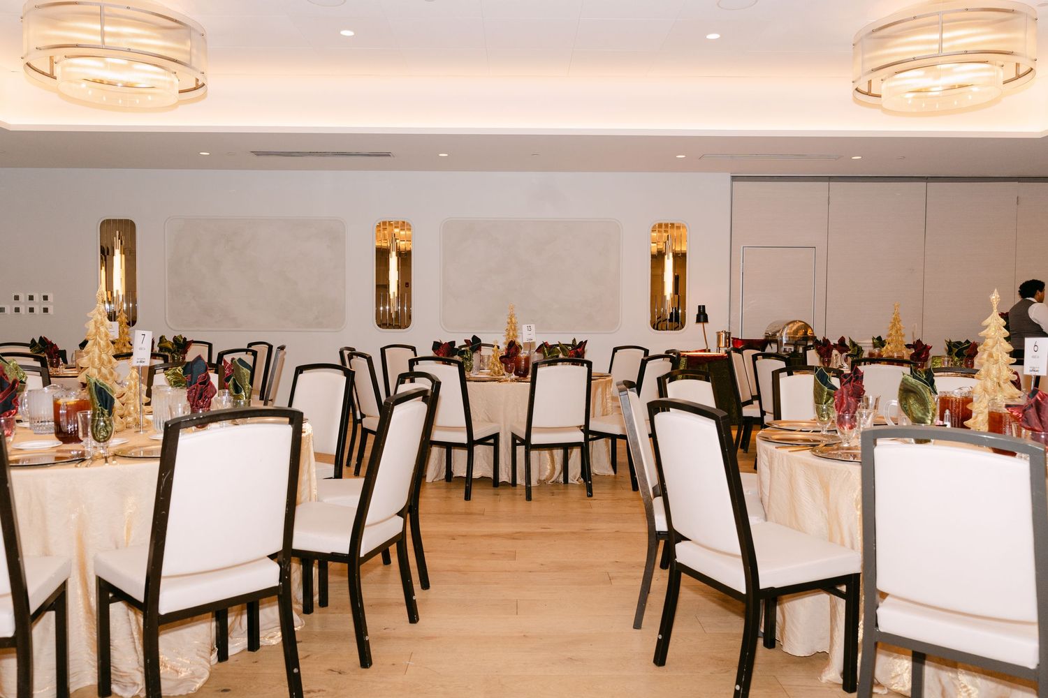 Modern restaurant interior with white tablecloths, dark chairs and circular pendant lighting fixtures overhead.