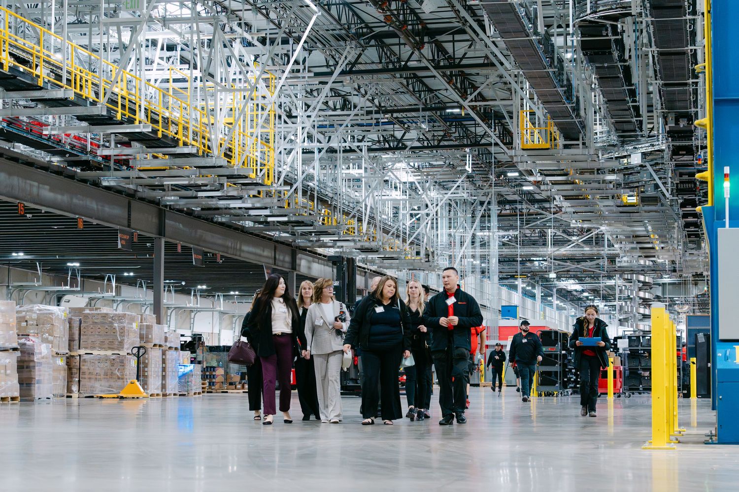 Large industrial warehouse interior with people walking through rows of shelving and equipment in a distribution facility.