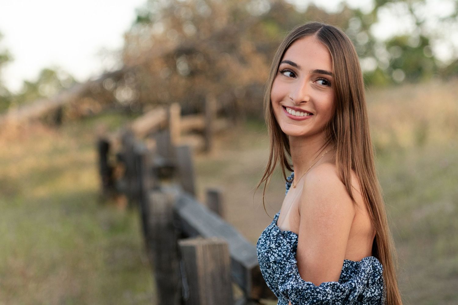 Woman in floral dress poses outdoors during golden hour photoshoot in natural setting.