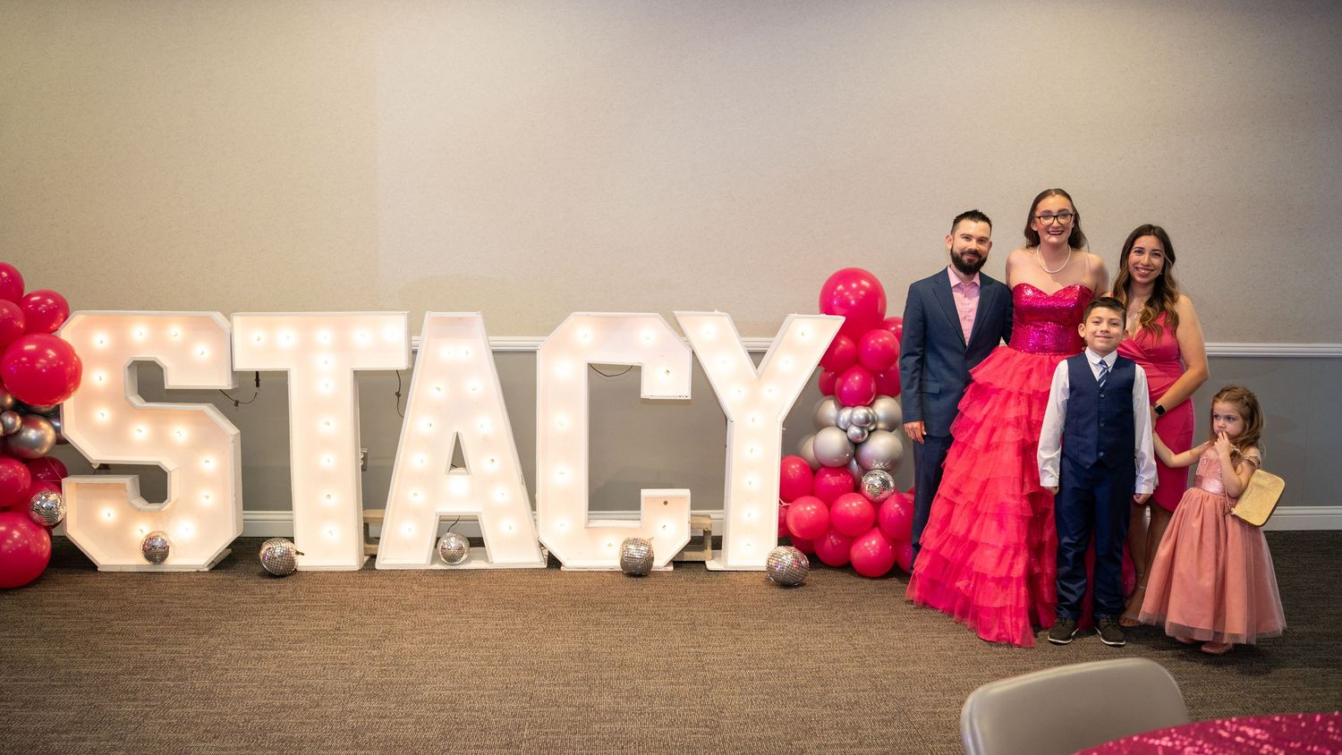 Large illuminated letter decorations spell out name against neutral wall with pink accents.
