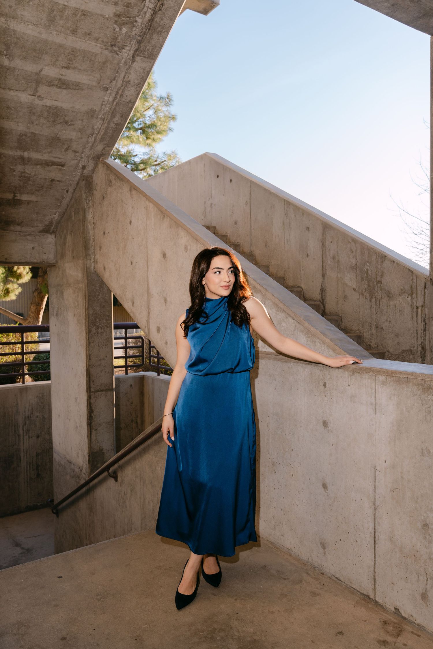 A series of artistic photos showing a person in a flowing blue dress posing against concrete architectural elements.