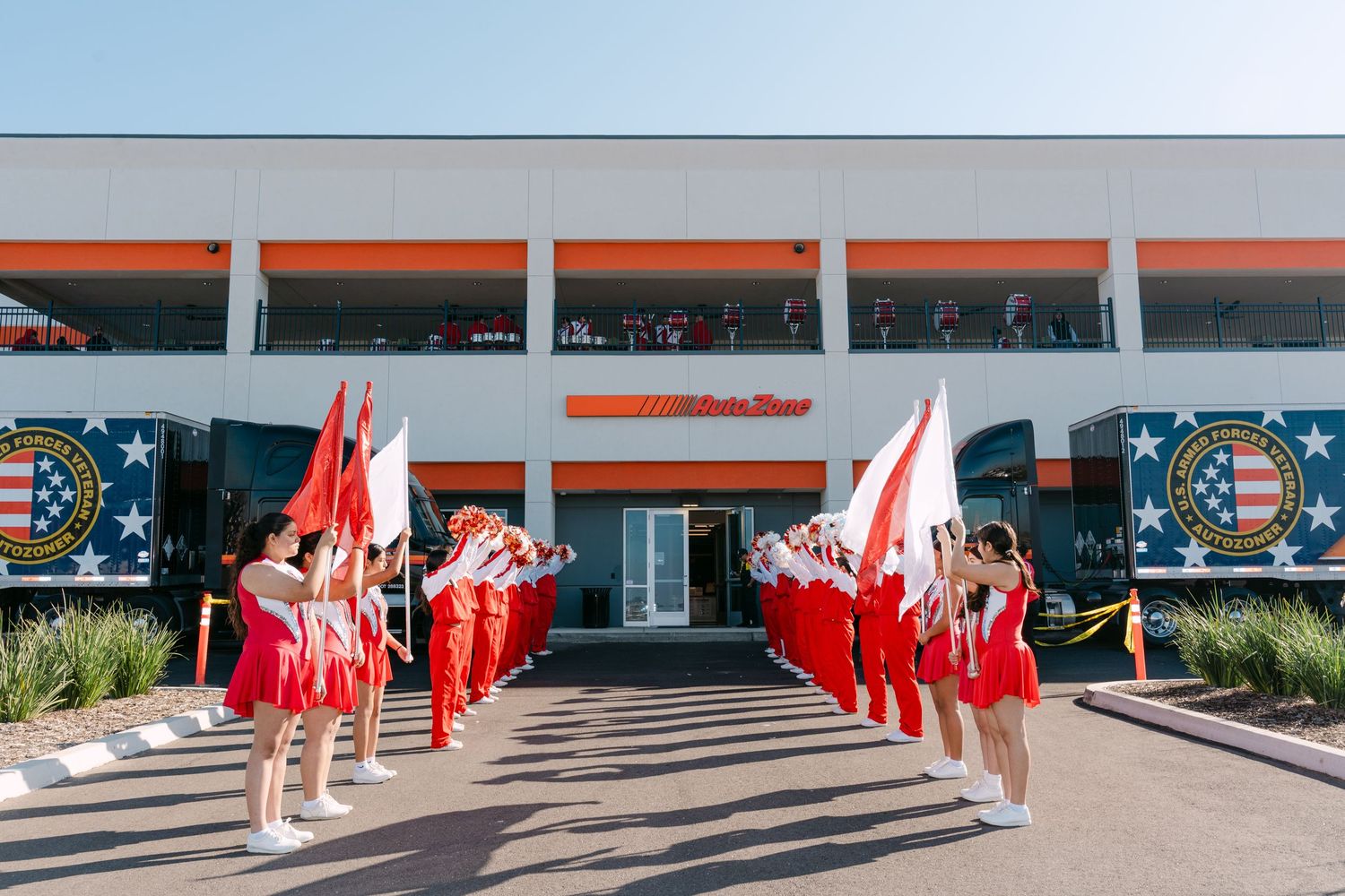Panoramic view of cheerleaders in red uniforms performing synchronized formations in front of a modern building.