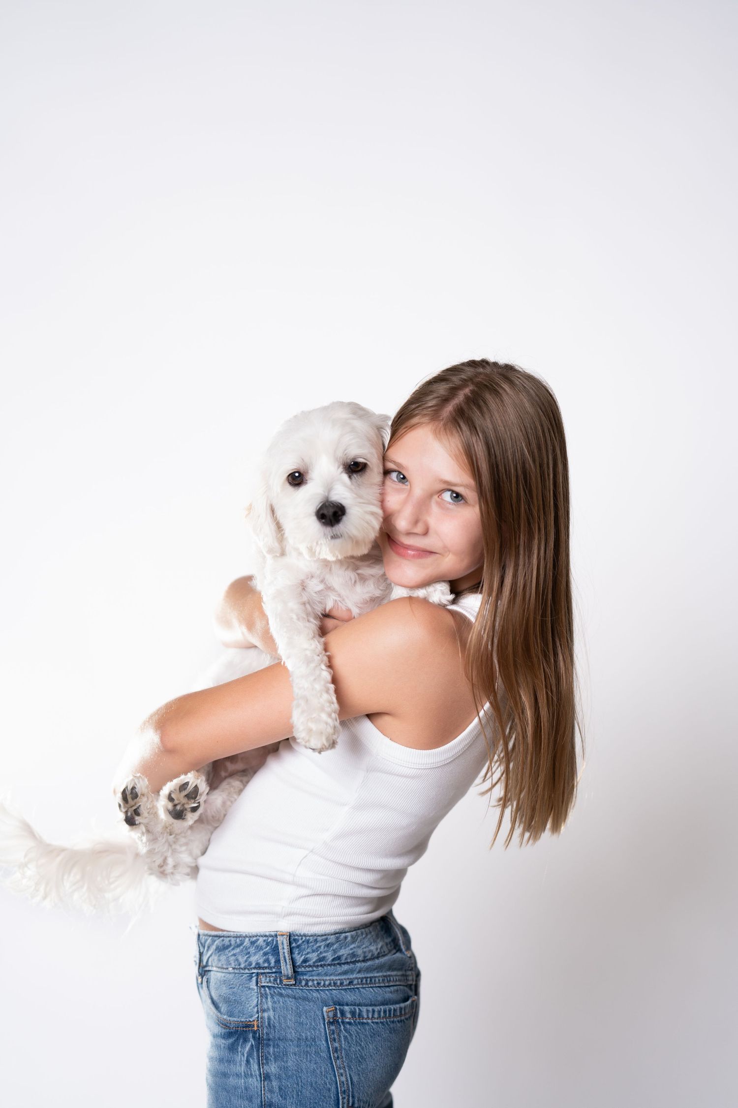 A person holds a small white fluffy dog while posing against a white background.