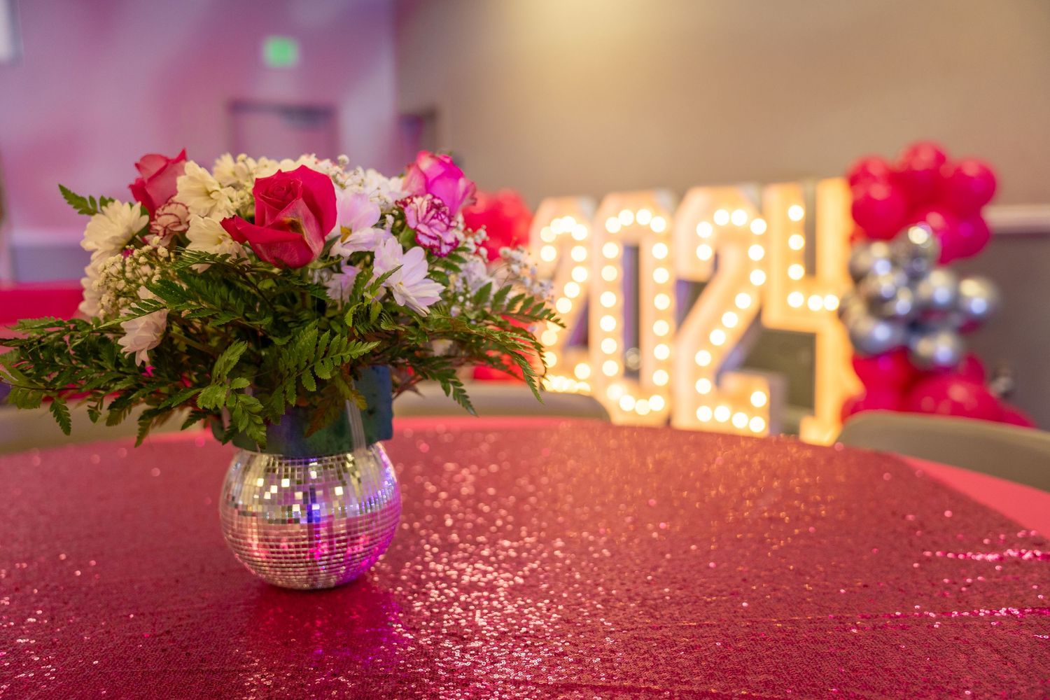 Pink glitter tablecloth with floral centerpieces and ambient lighting creates romantic party setting.