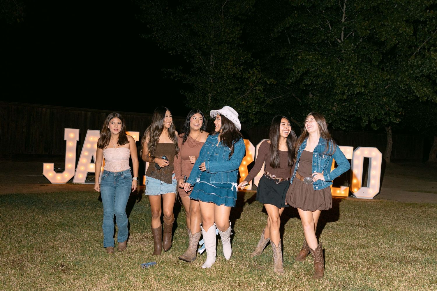 Group of people sitting outdoors at night on wooden benches arranged in a curved formation.
