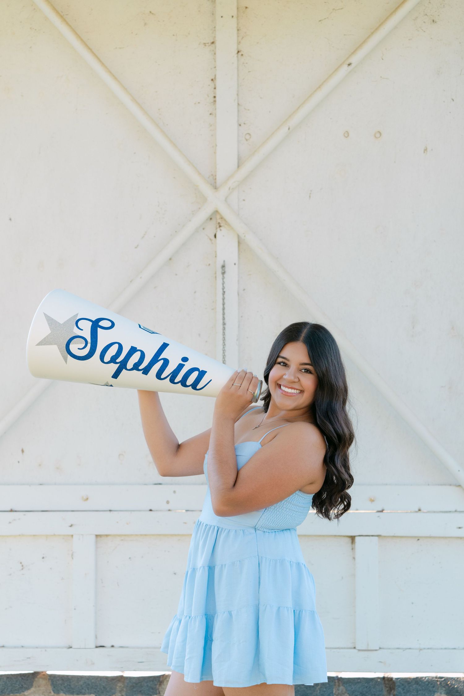 Smiling young woman in light blue dress holding a personalized megaphone with the name Sophia outdoors.