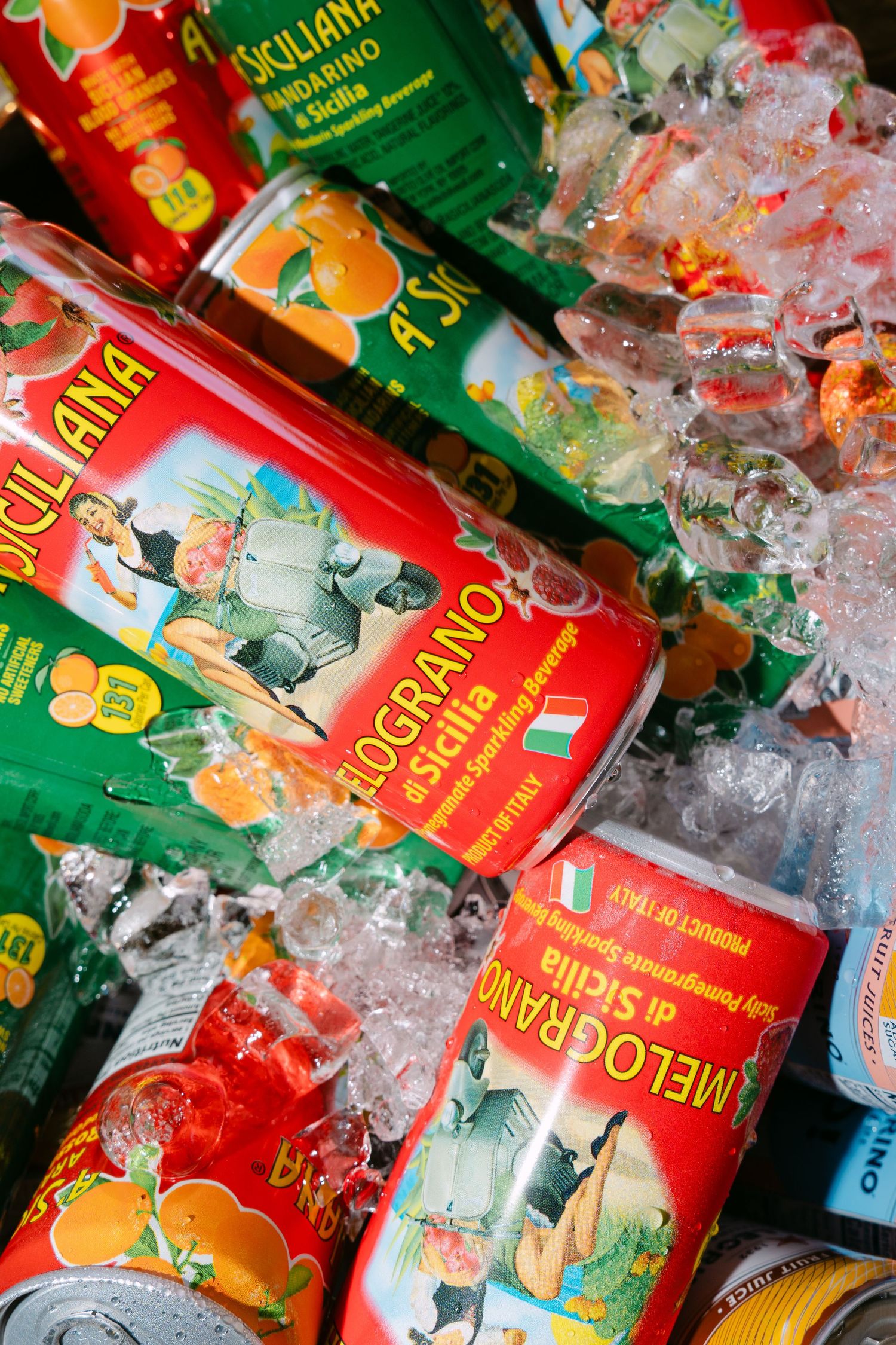 Colorful Italian Siciliana and Melograno di Sicilia beverage cans chilled on ice, featuring vibrant fruit-themed labels.
