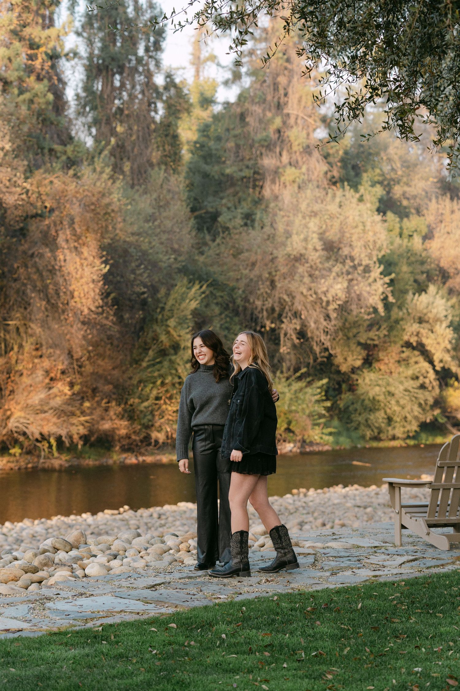 Two people stand by a lake surrounded by autumn trees and foliage.