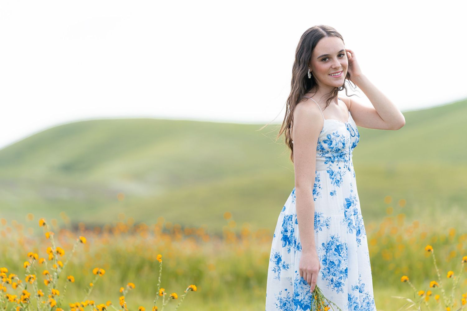 Outdoor fashion photography in rolling hills with yellow wildflowers and natural lighting.