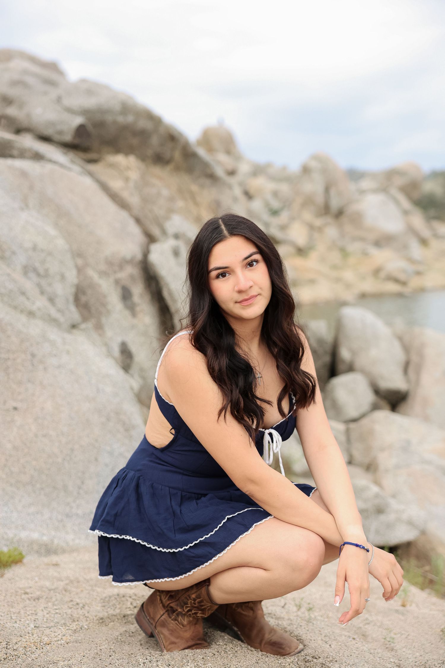 Woman in navy dress poses on rocky beach landscape during outdoor photoshoot.