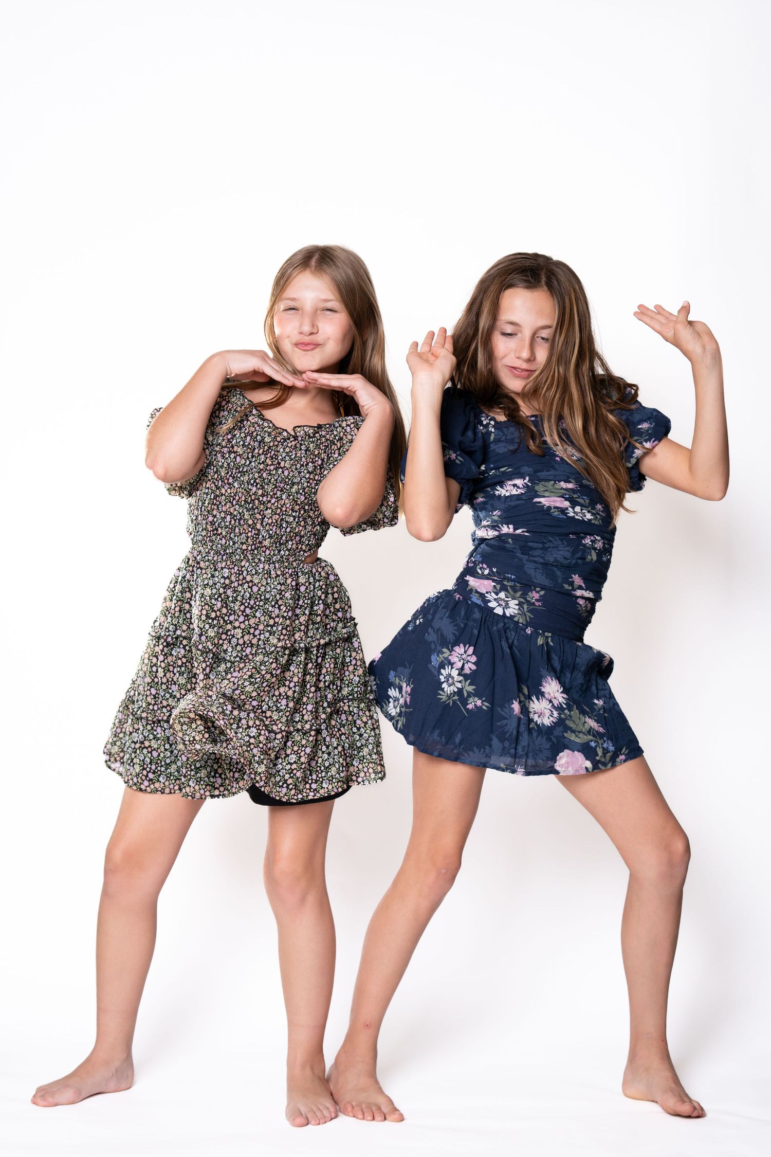 Playful dance poses in floral and navy dresses against white backdrop.