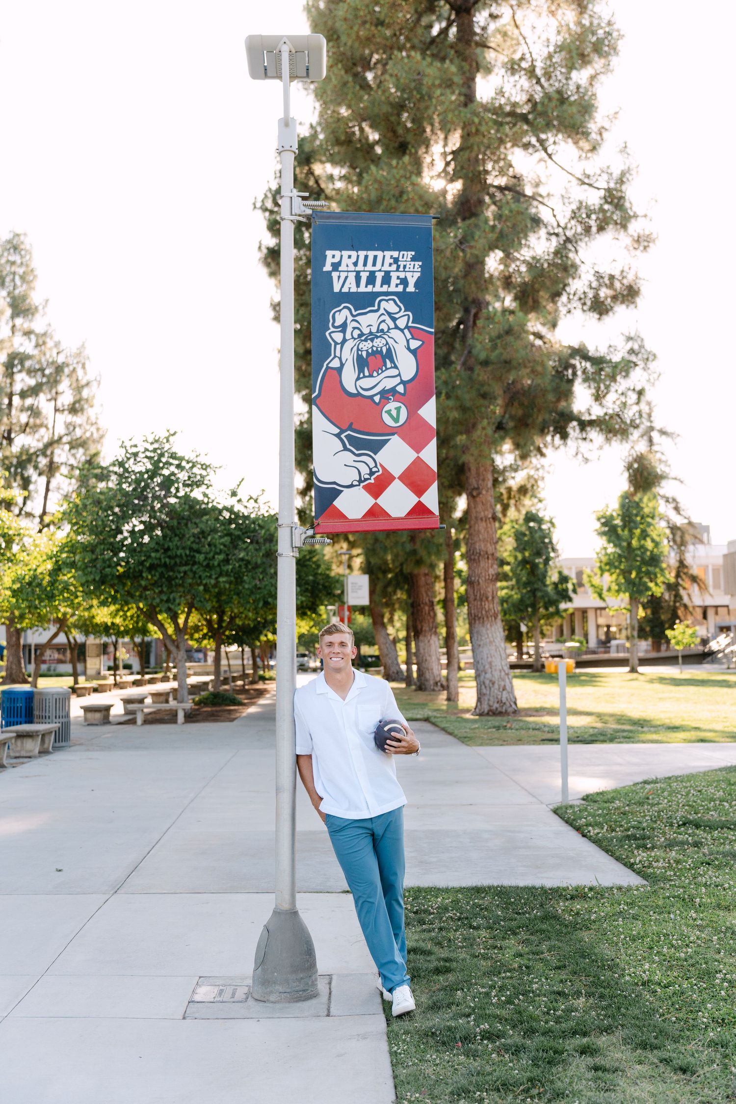 Student leaning against a lamppost with a Fresno State Bulldogs Pride of the Valley banner on a sunny campus.