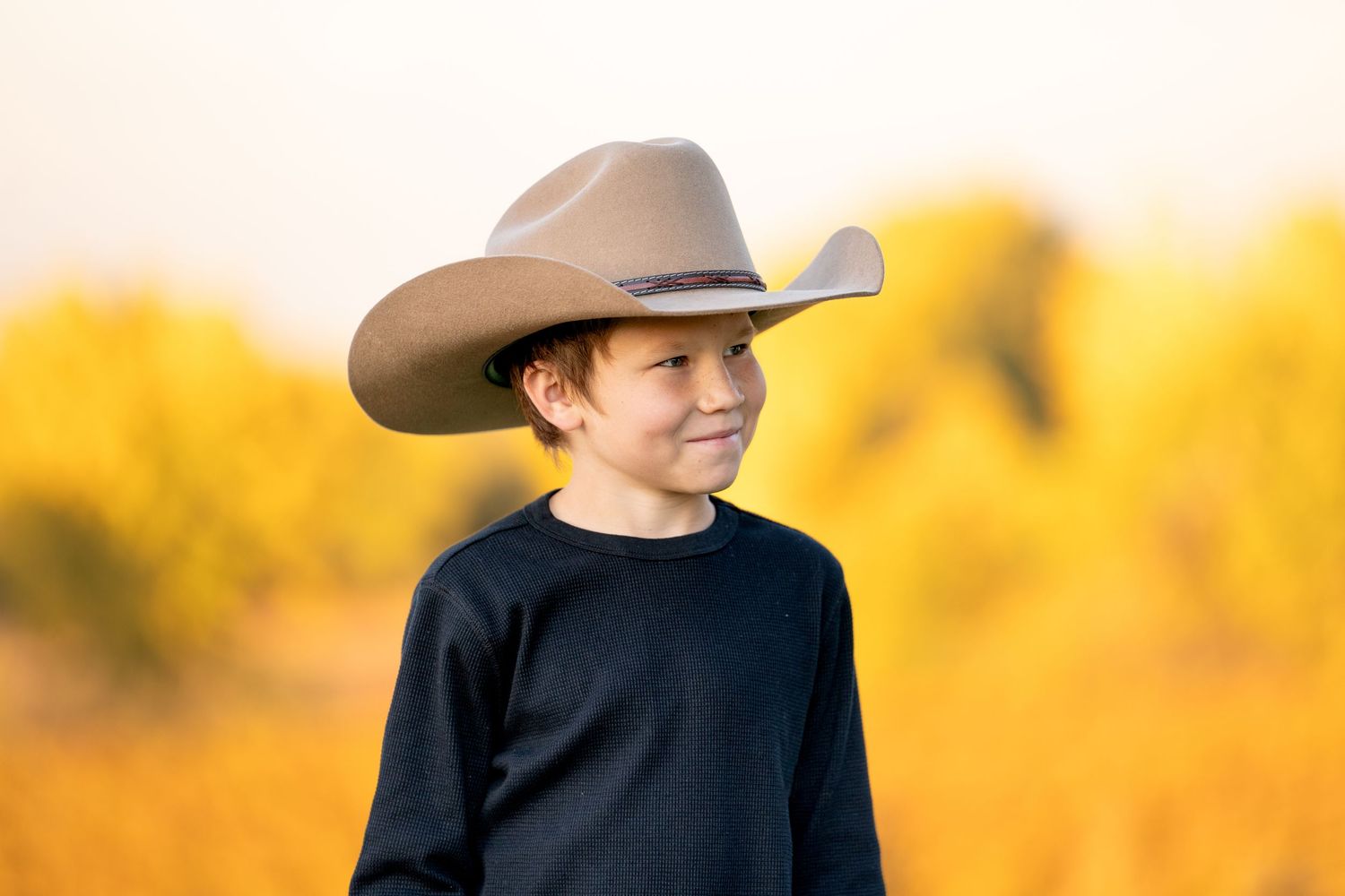 A young person wearing a cowboy hat and black sweater against a golden sunset background.