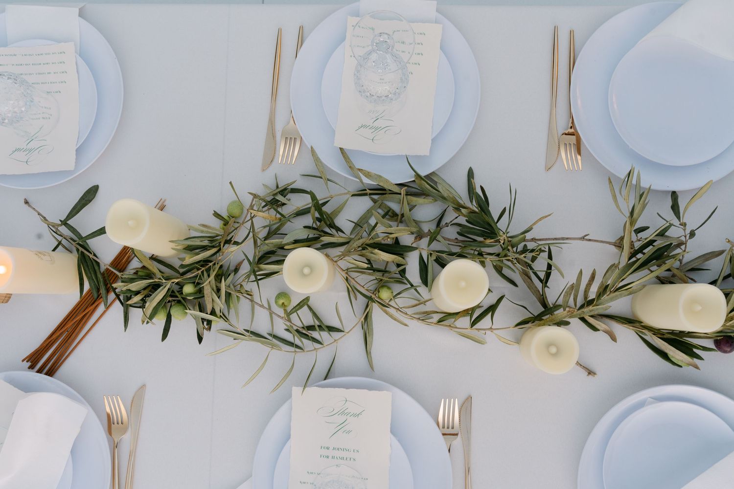 Elegant white table setting with olive branches and white roses as centerpiece decorations.