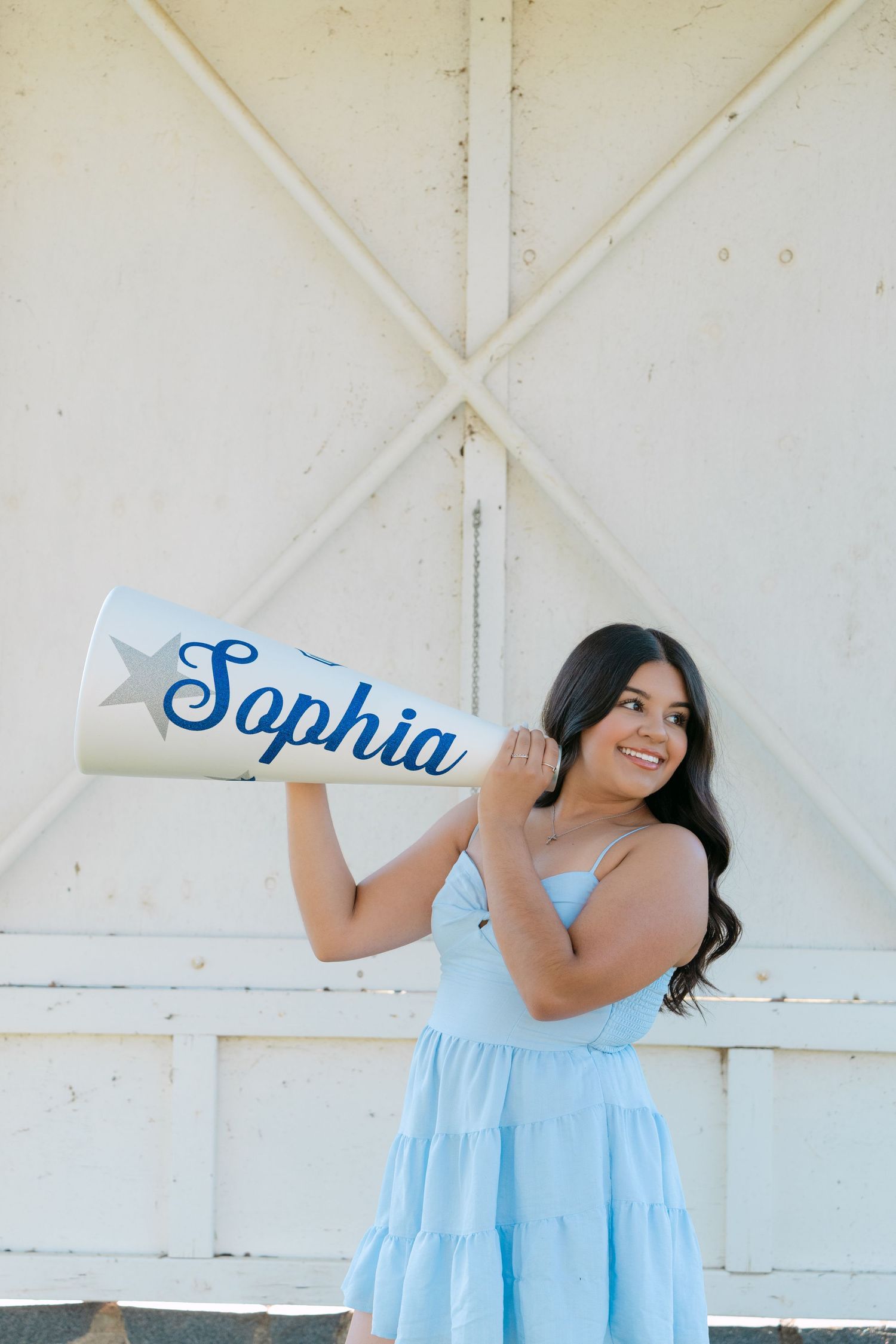 Young woman in light blue dress holding a personalized white megaphone with the name Sophia outdoors.
