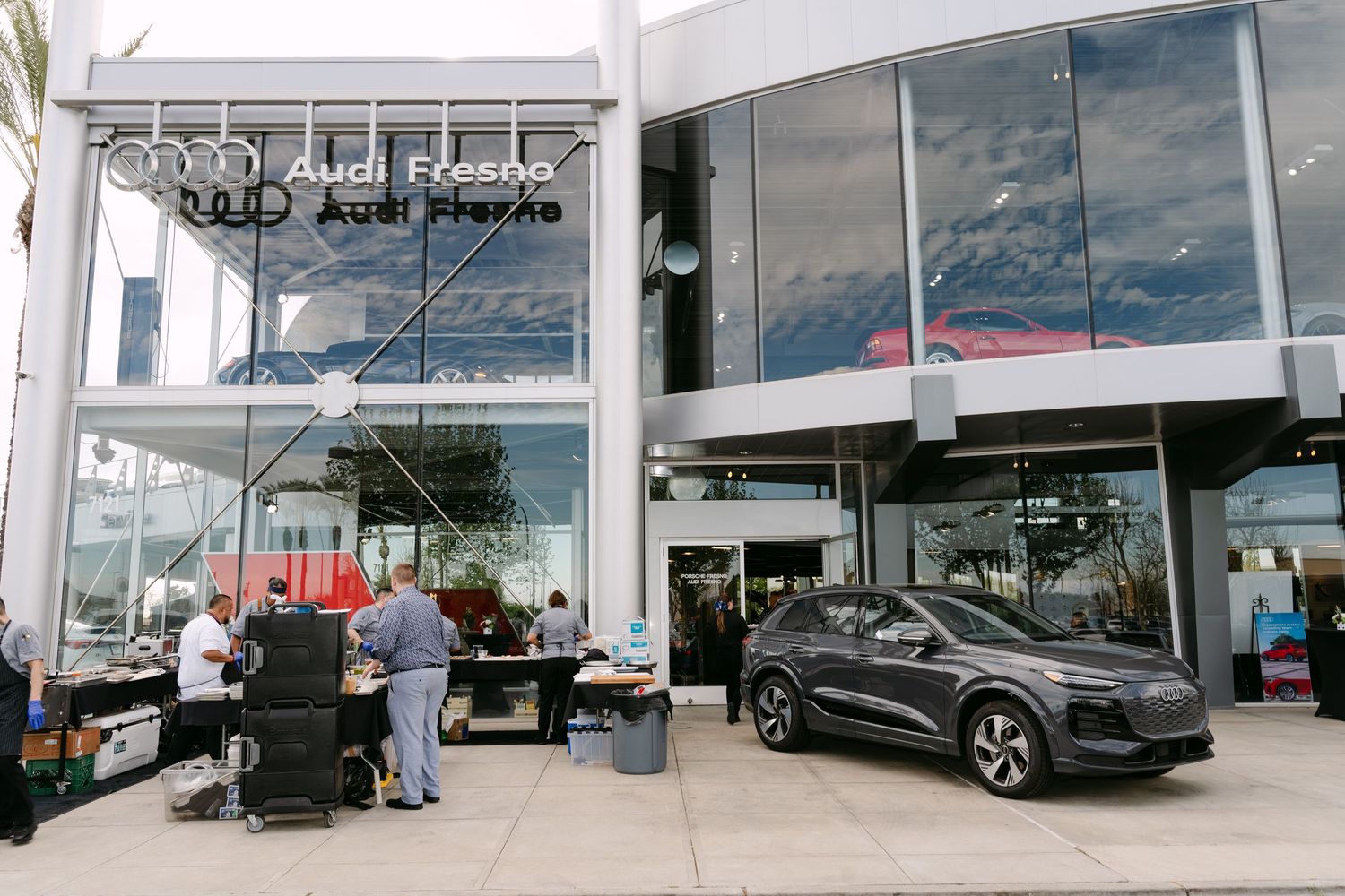 Modern car dealership exterior with glass windows reflecting cloudy sky.