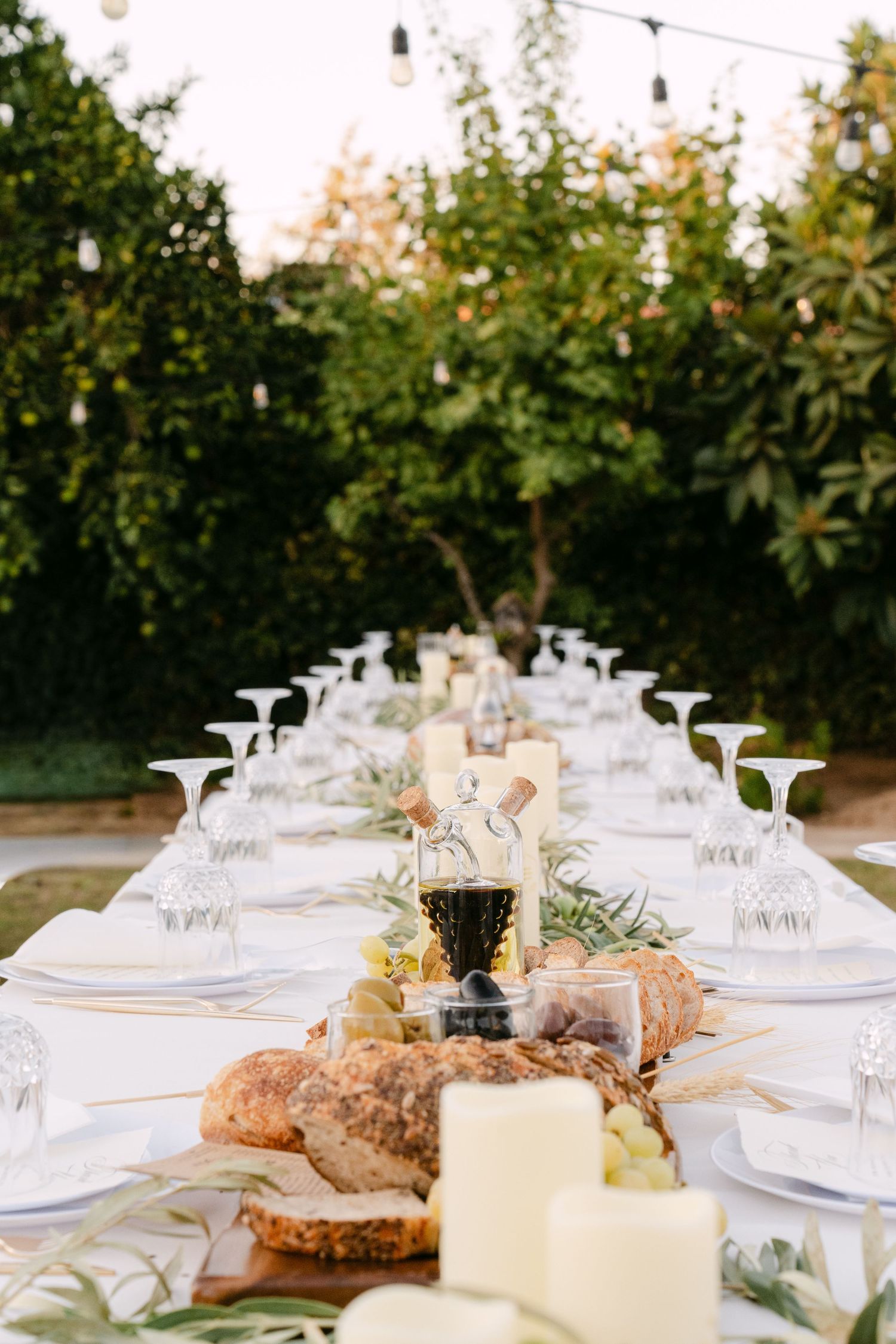 Intimate outdoor dinner party setup with string lights and elegant white table settings.