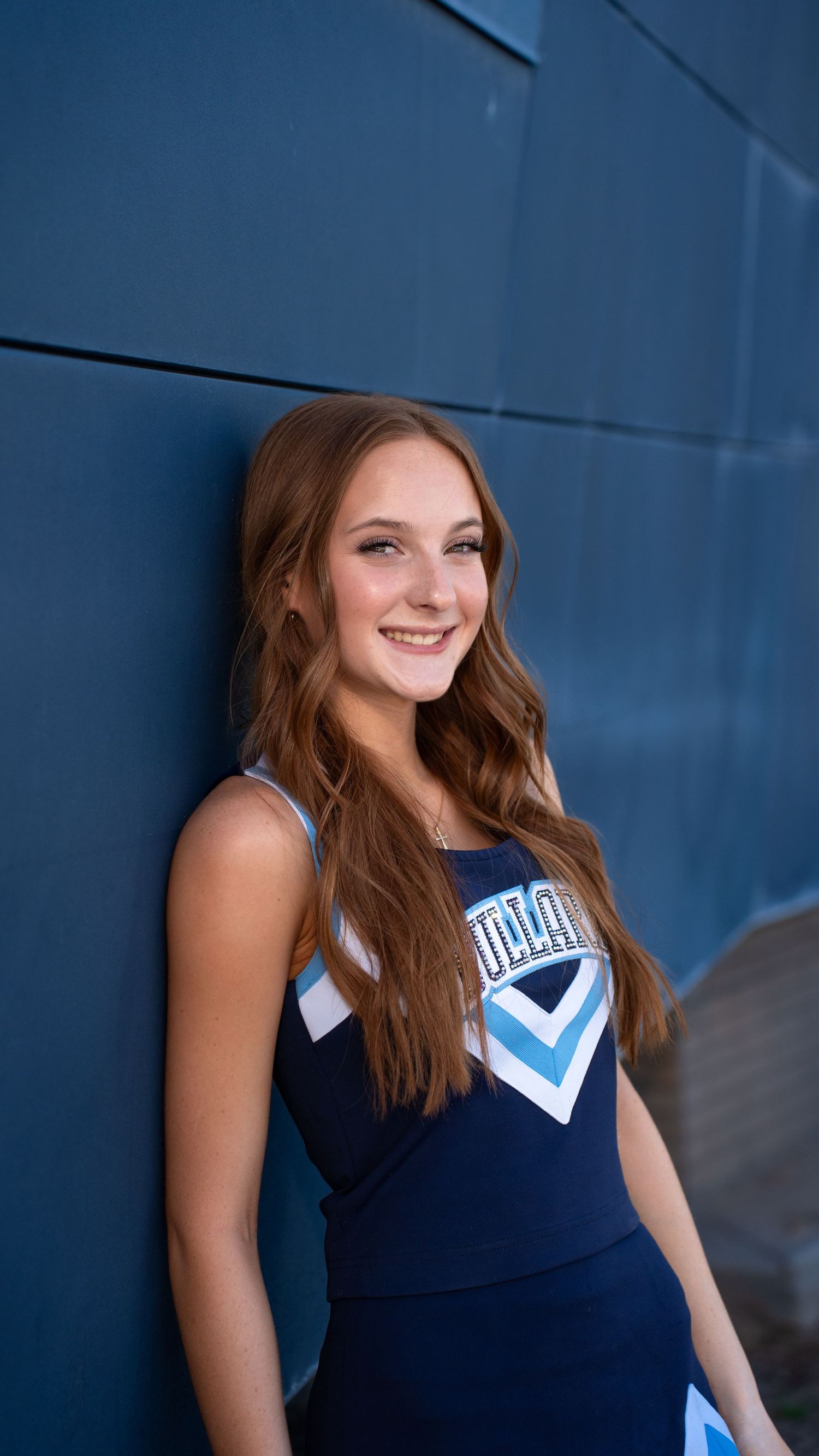 Cheerleader poses against blue wall wearing navy uniform with white chevron design.