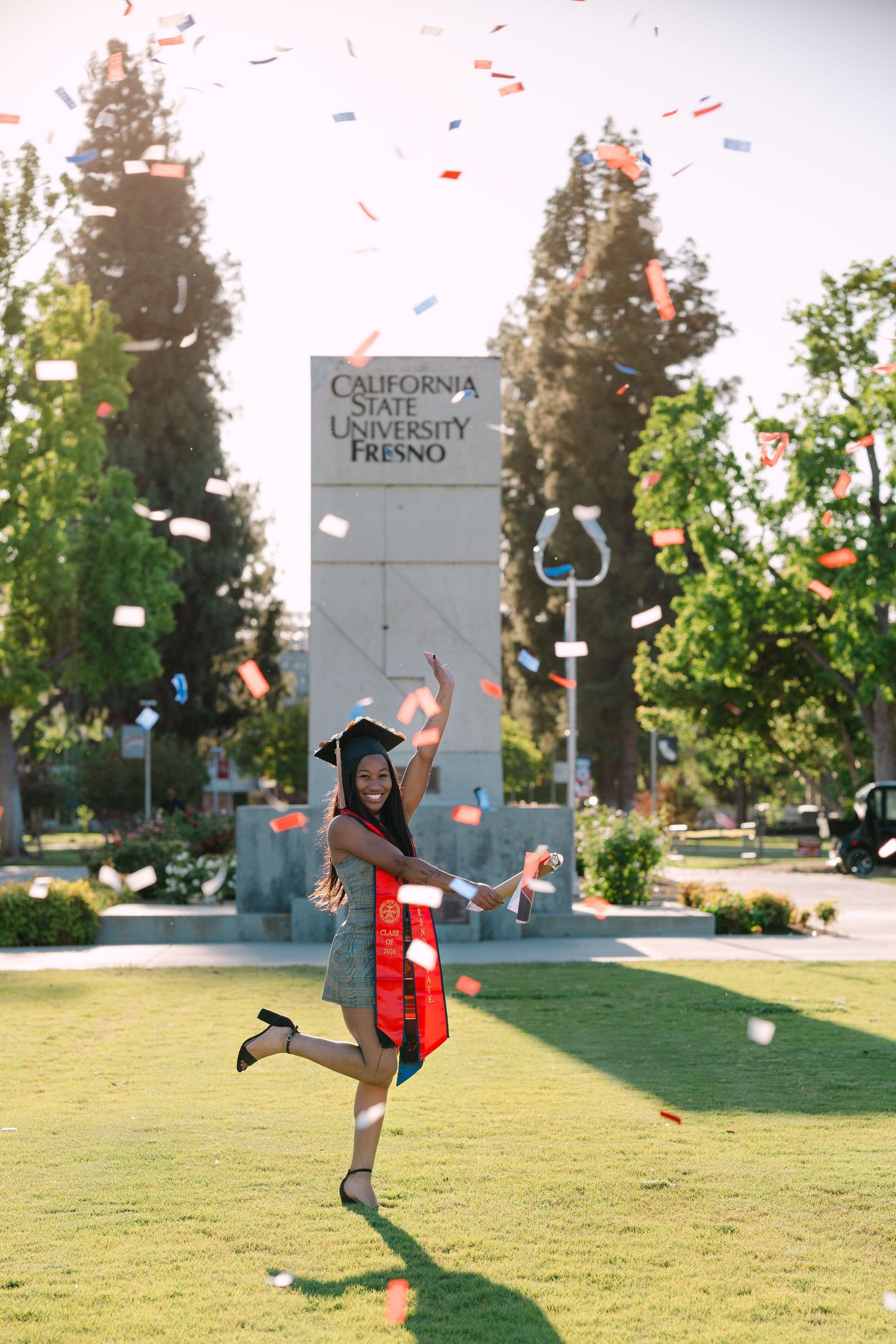 Joyful graduate celebrates in cap and gown at California State University Fresno with colorful confetti.