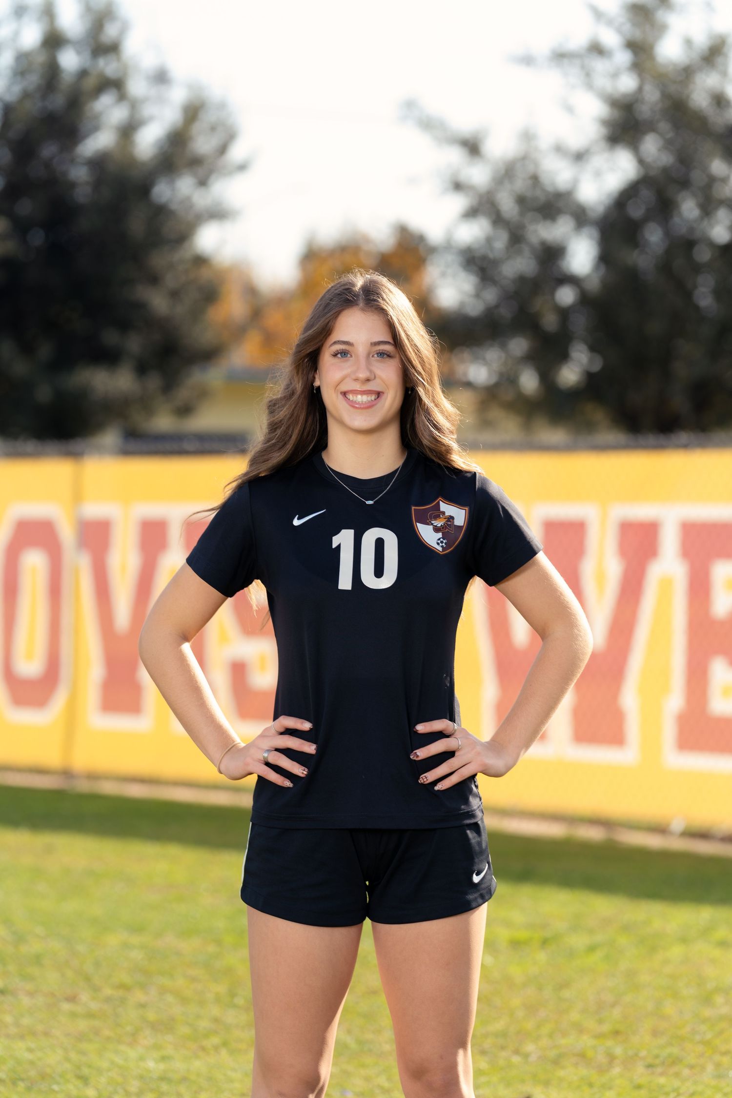 Soccer player in black Nike jersey stands on field with number 10 uniform during outdoor sports photoshoot.