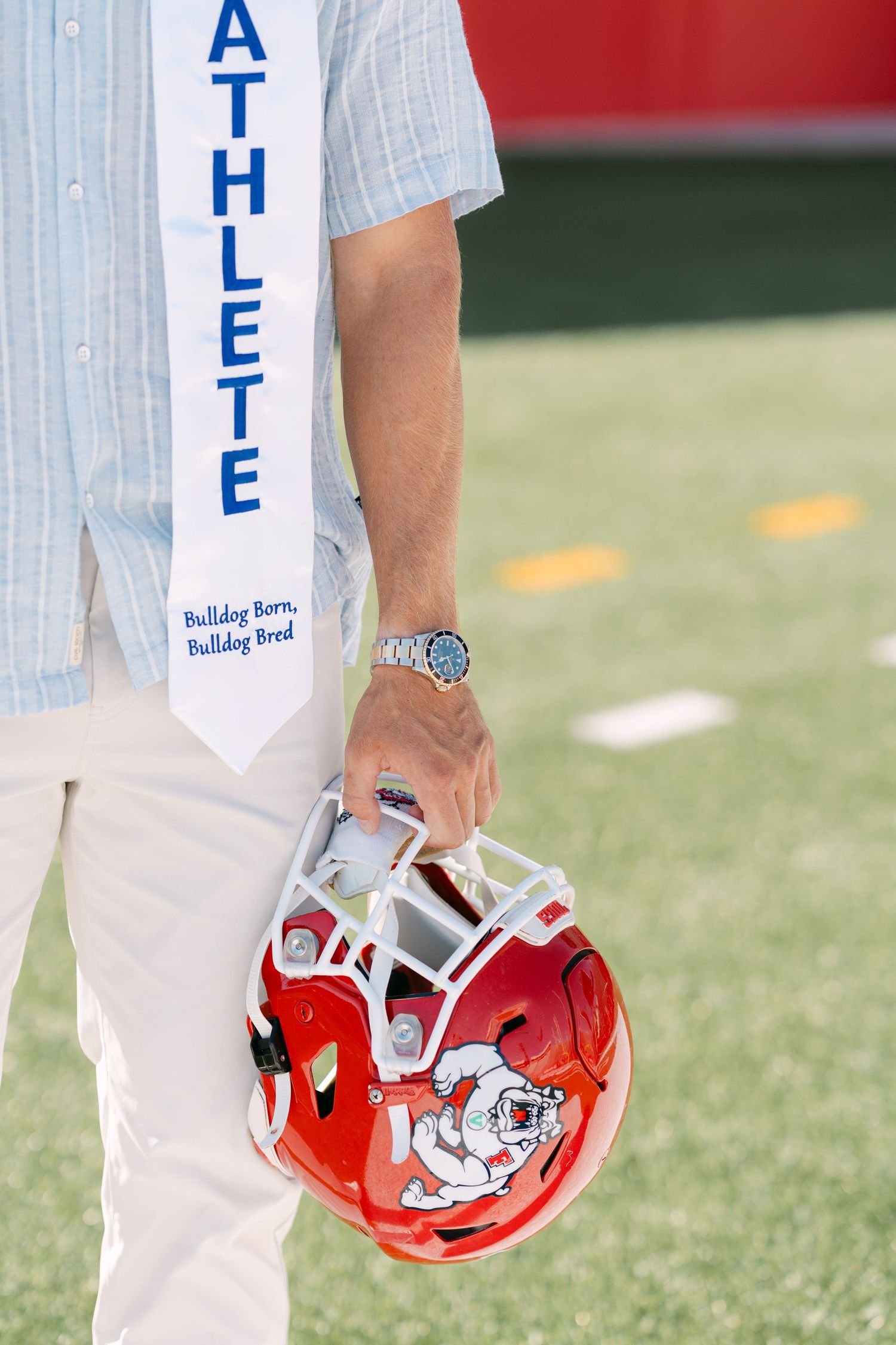 Fresno State student-athlete holds red Bulldog helmet wearing graduation stole reading Athlete and Bulldog Born Bulldog Bred.