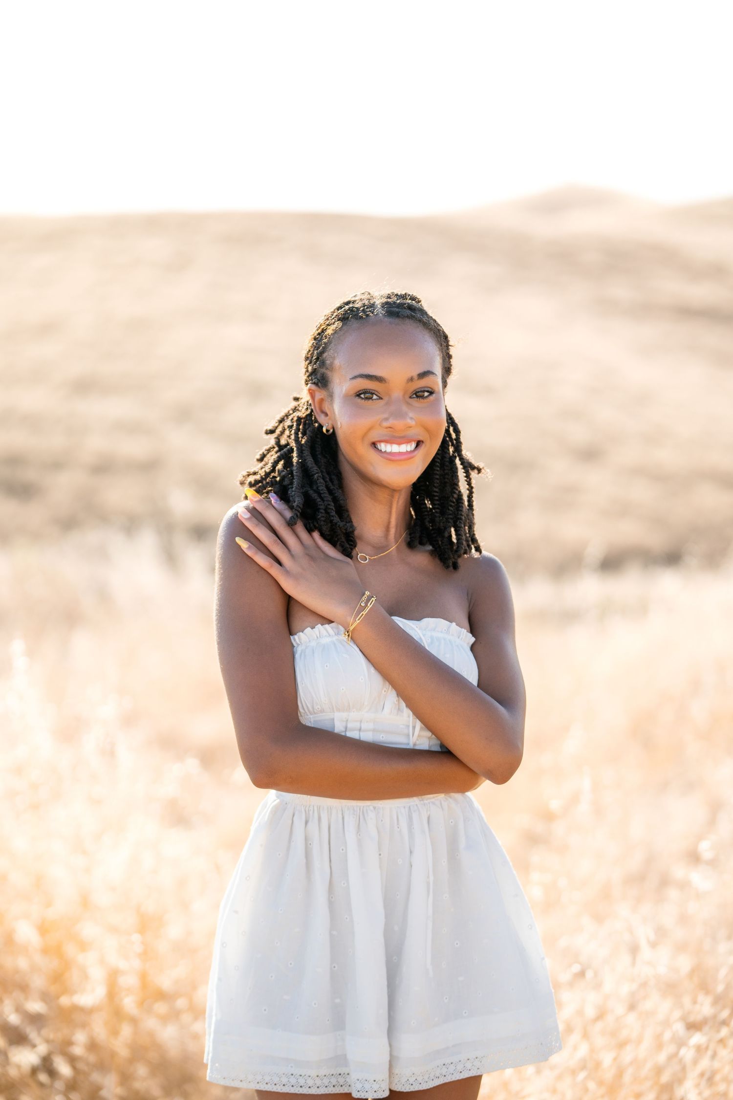 Person in white summer dress poses joyfully in golden wheat field at sunset.