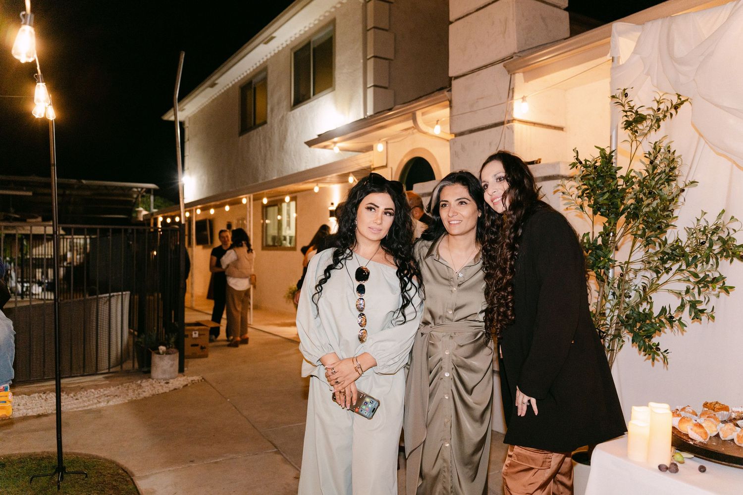 People gathered at an outdoor evening event with string lights and white decor.