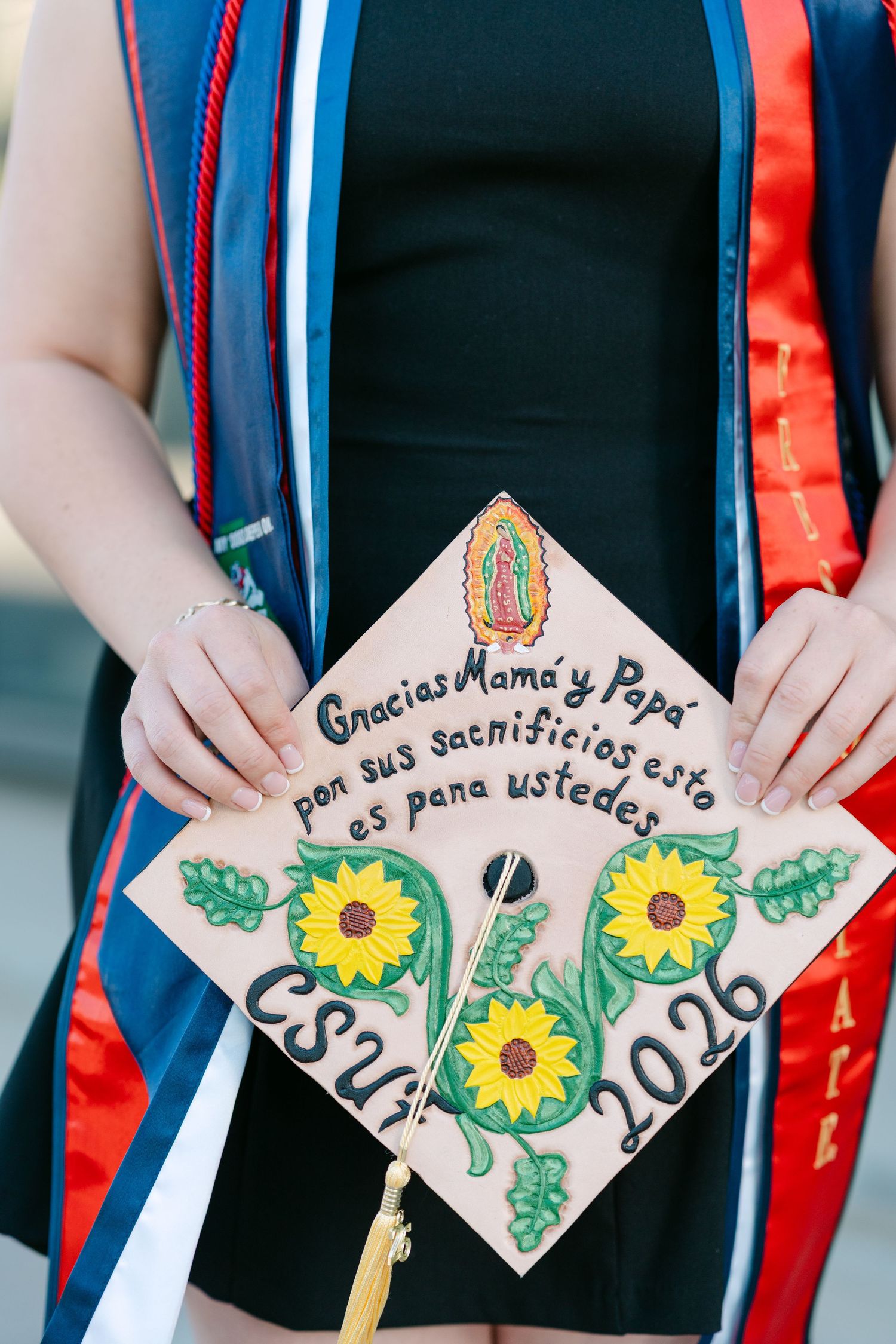 CSUN 2026 graduation cap decorated with sunflowers and Spanish text thanking parents, held by graduate in regalia.